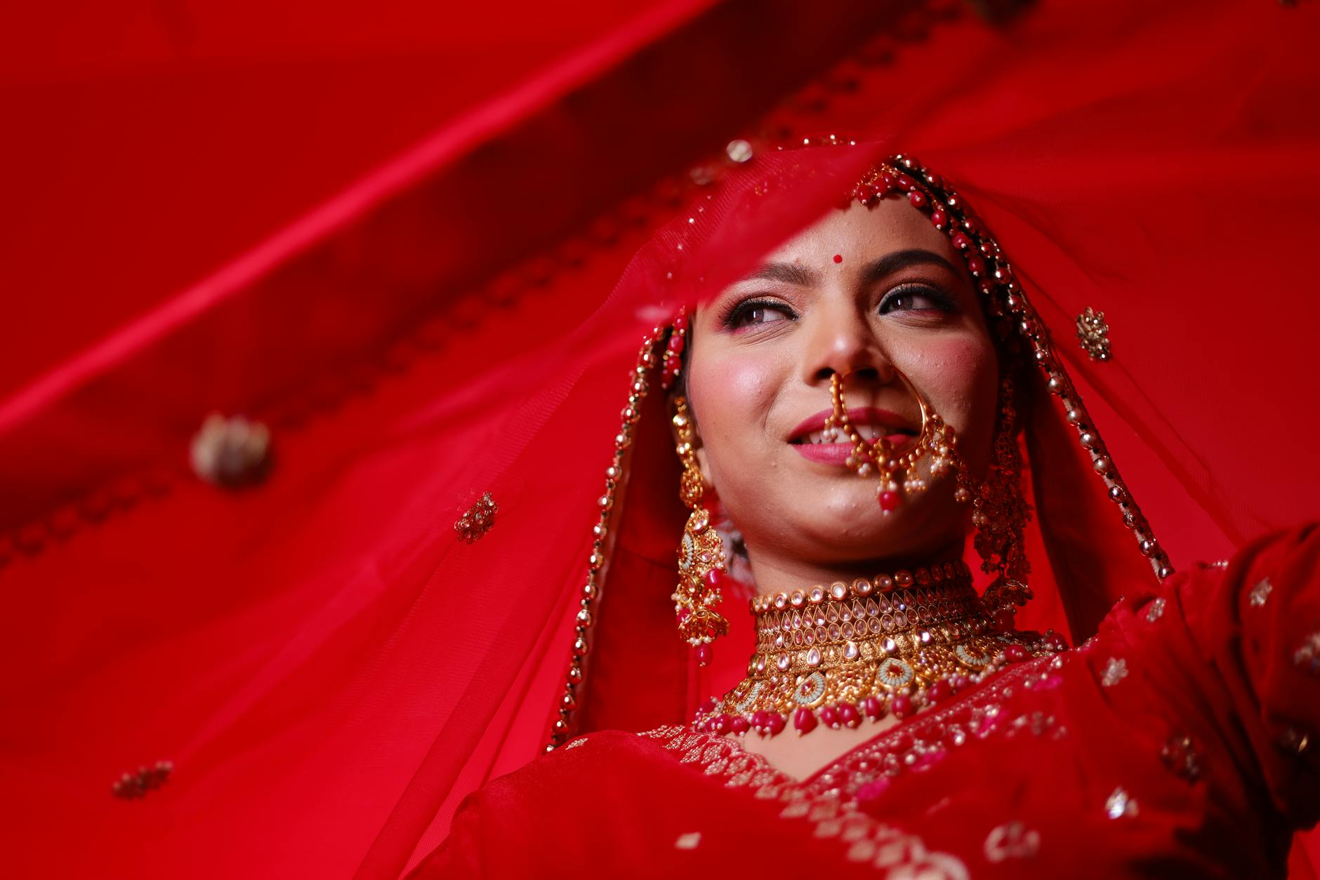 Portrait of a beautiful Indian bride wearing traditional jewelry, captured in vibrant red hues.