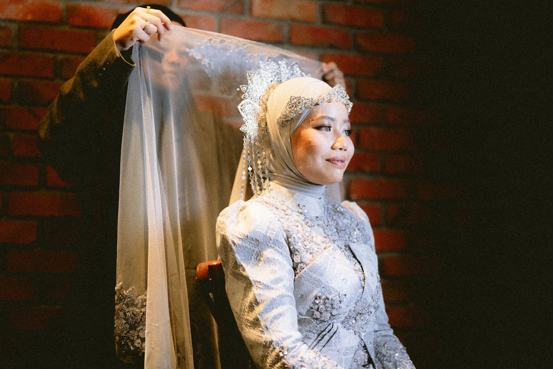 A beautiful bride in silver attire during a traditional indoor ceremony against a brick wall.
