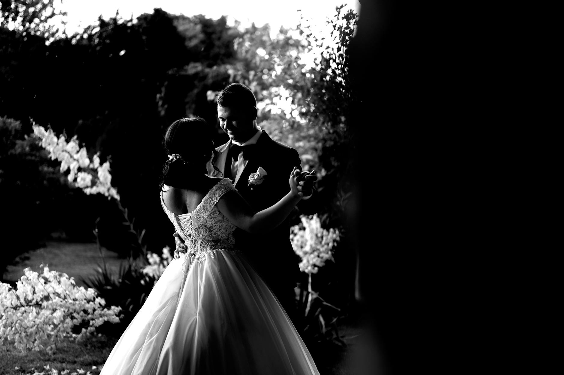 A romantic black and white photo of newlyweds dancing together outdoors.
