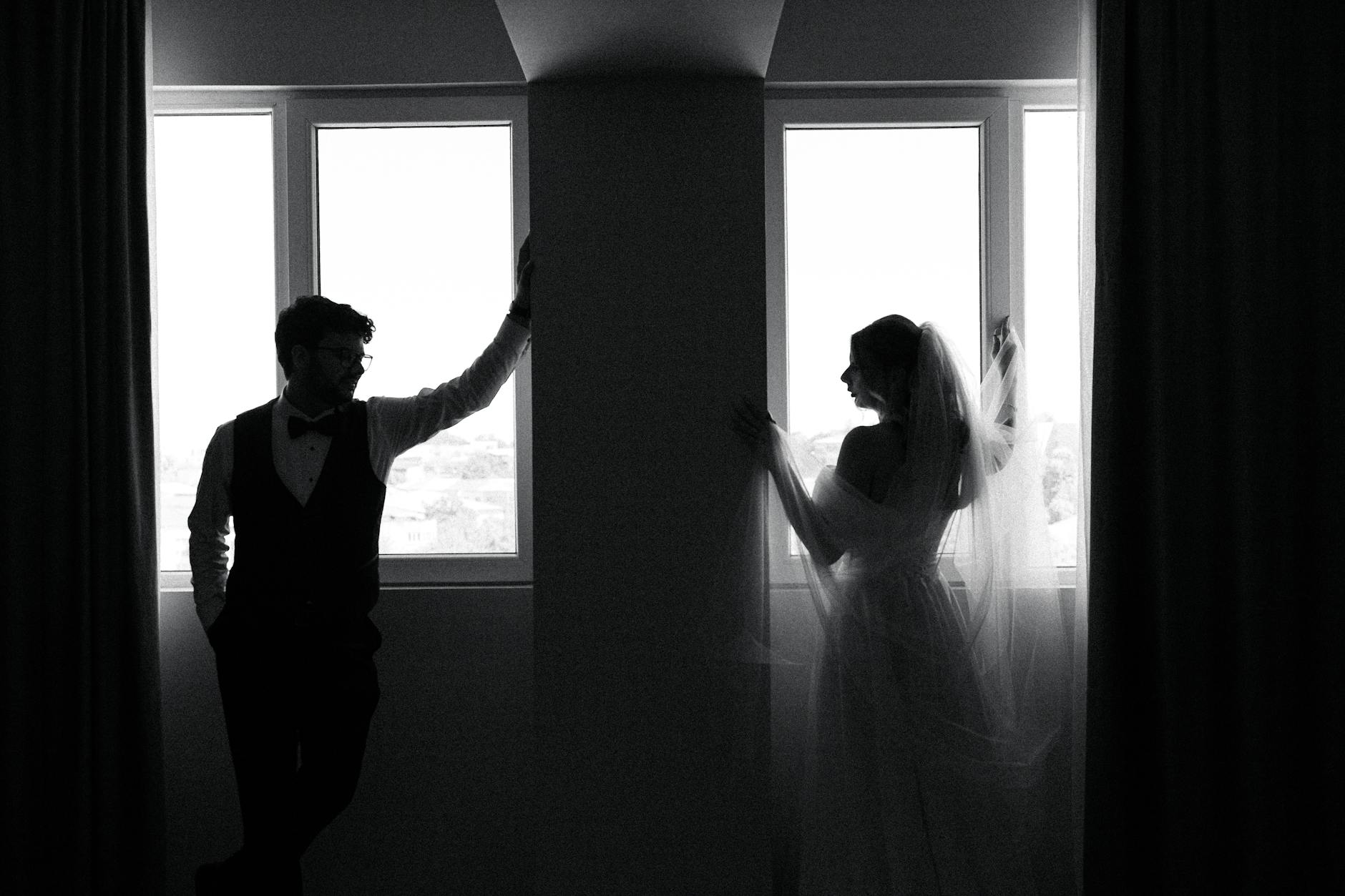Black and white silhouette of a bride and groom by a window, creating a timeless and elegant look.