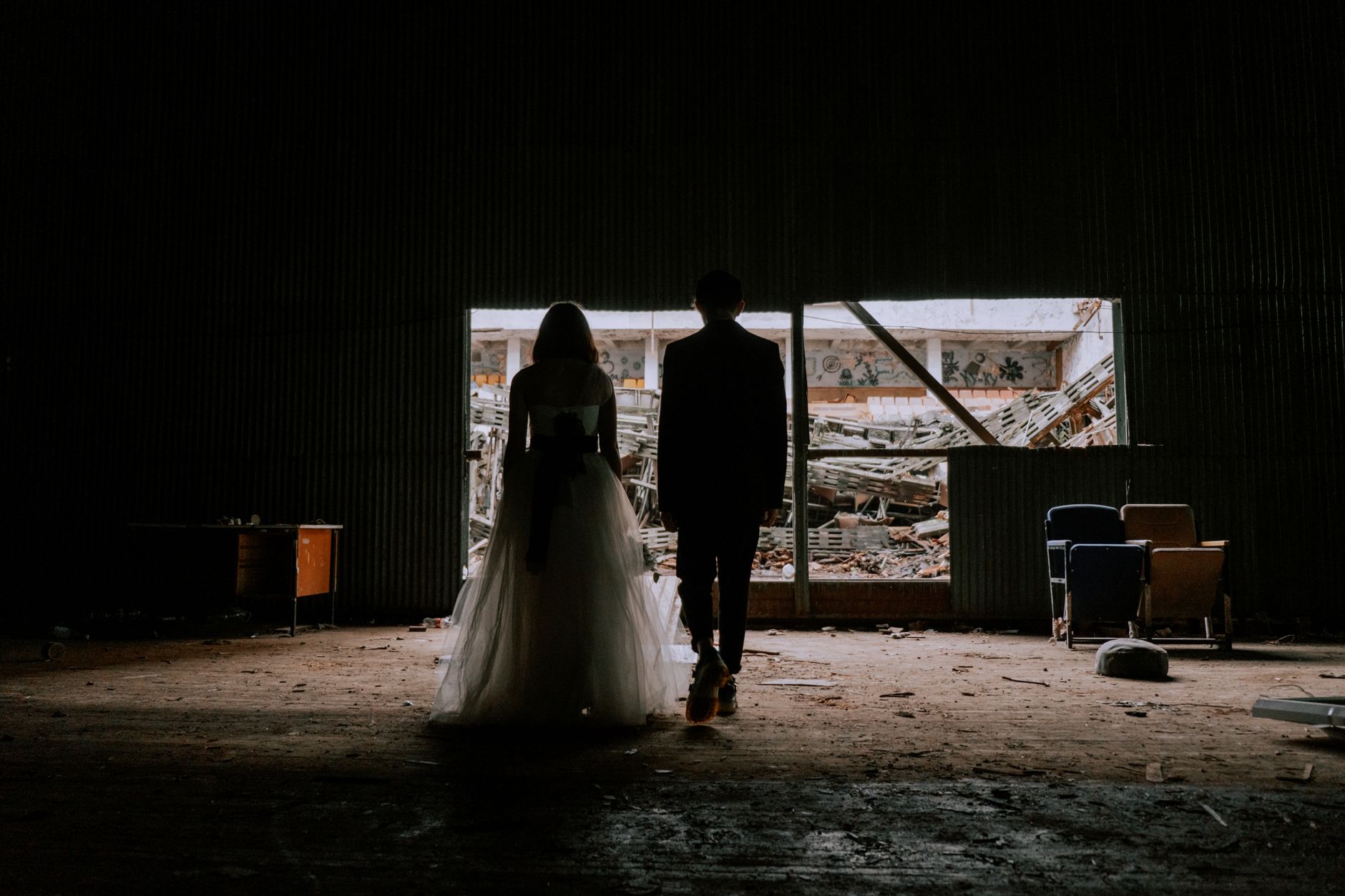A bride and groom stand in a dark, deserted building, creating a dramatic silhouette.
