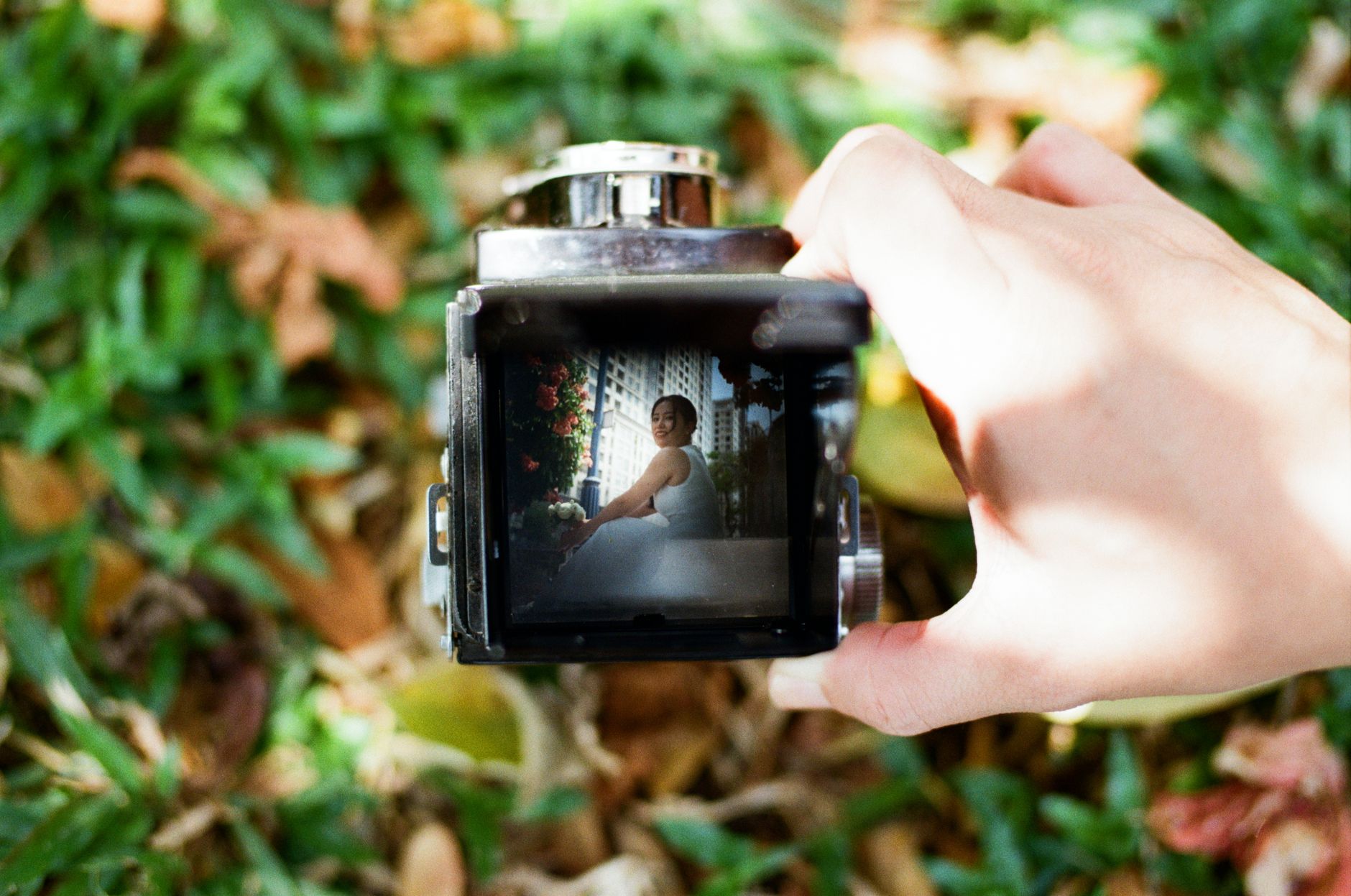 A unique view of a bride through a vintage camera with grass background.