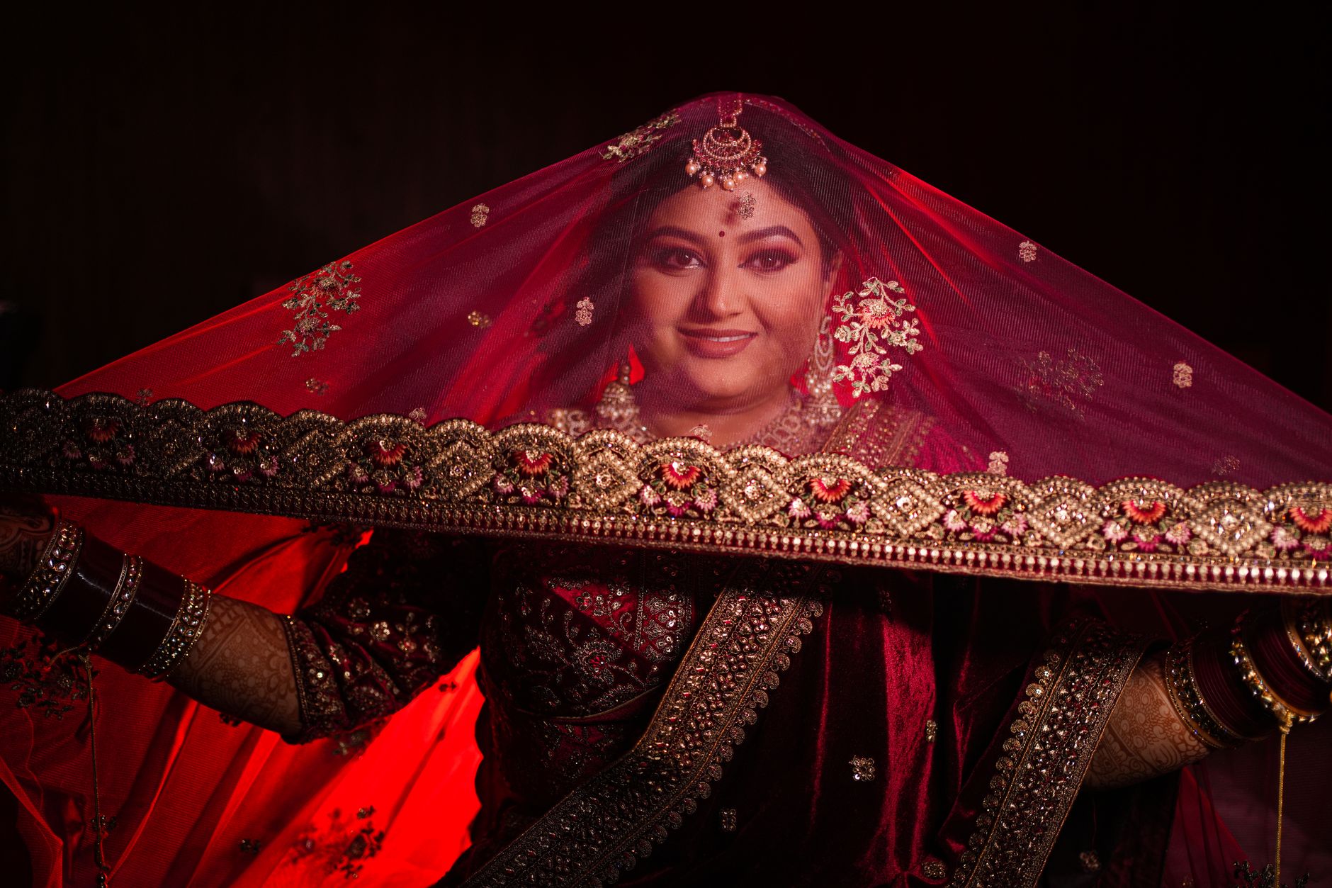 Stunning portrait of an Indian bride in red veil adorned with traditional jewelry.