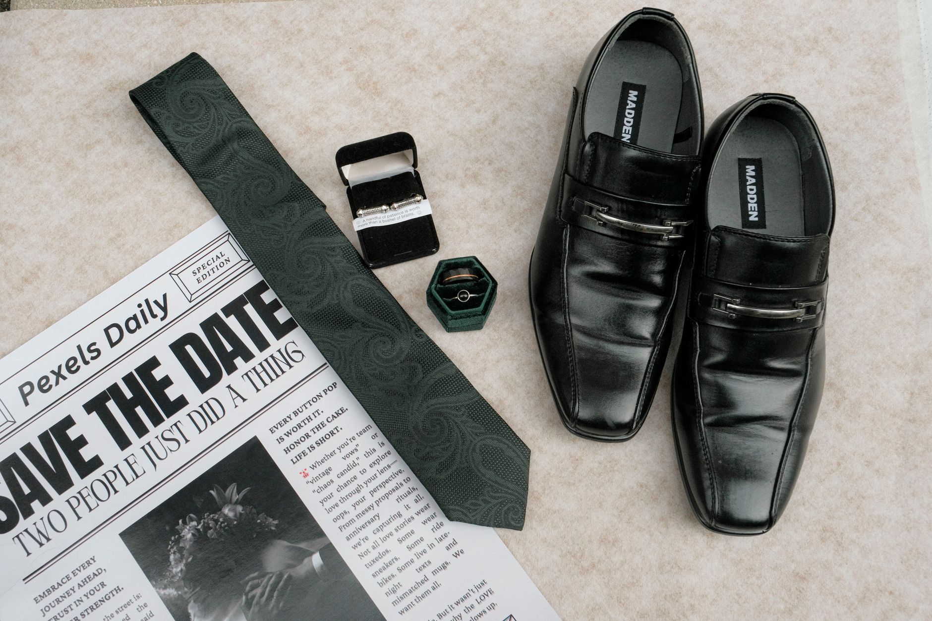 Flat lay of wedding accessories including shoes, tie, and rings on a newspaper background.