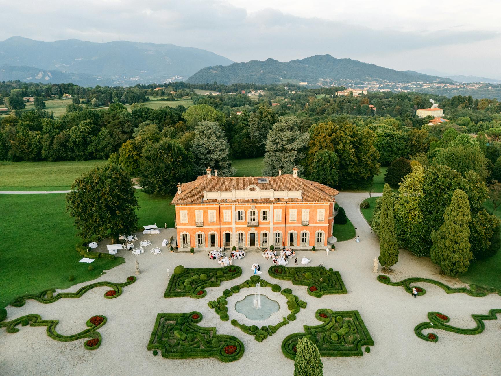 A stunning aerial view of a historic villa and gardens in Italy, surrounded by lush greenery.