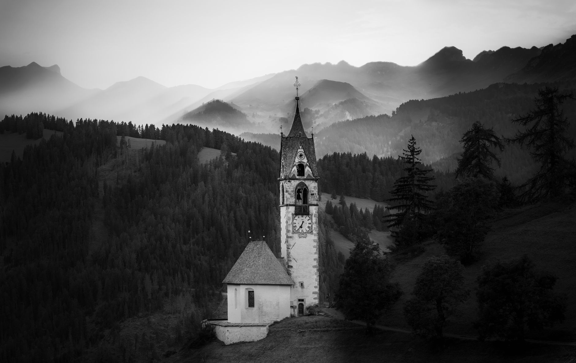 A serene black and white image of a chapel nestled in misty Dolomites, Italy.