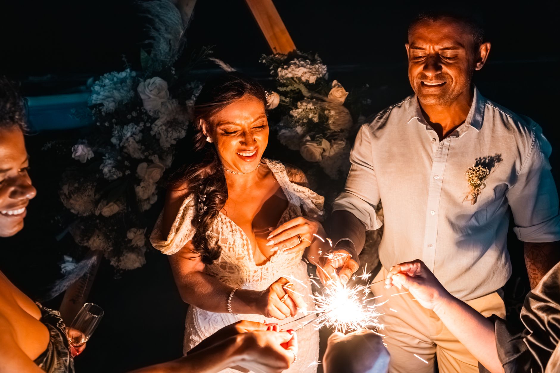 A joyous wedding couple celebrates with sparklers under the night sky.