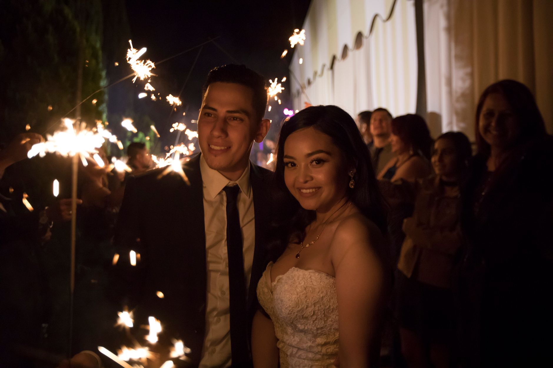 Joyful wedding couple celebrating with sparklers surrounded by guests.