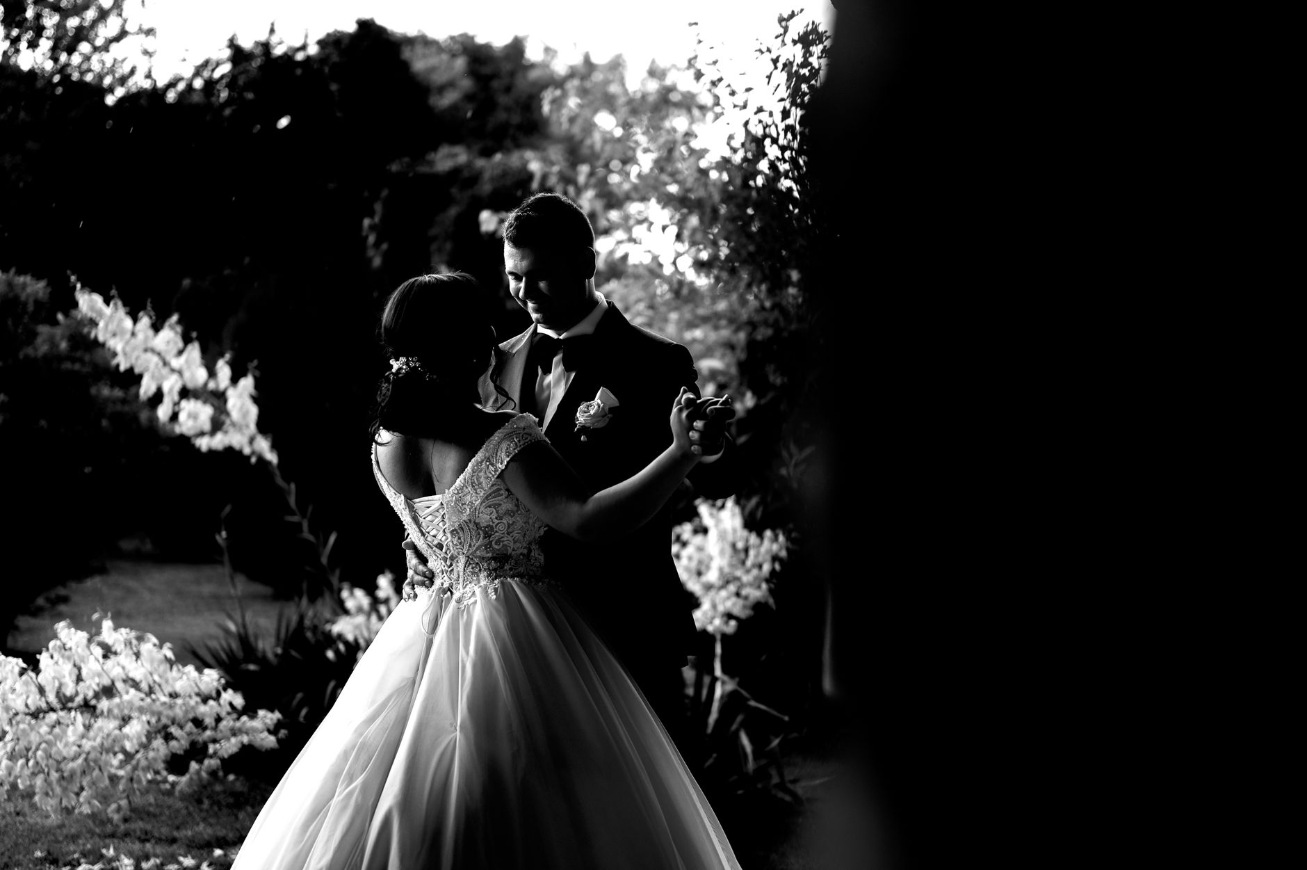 A romantic black and white photo of newlyweds dancing together outdoors.