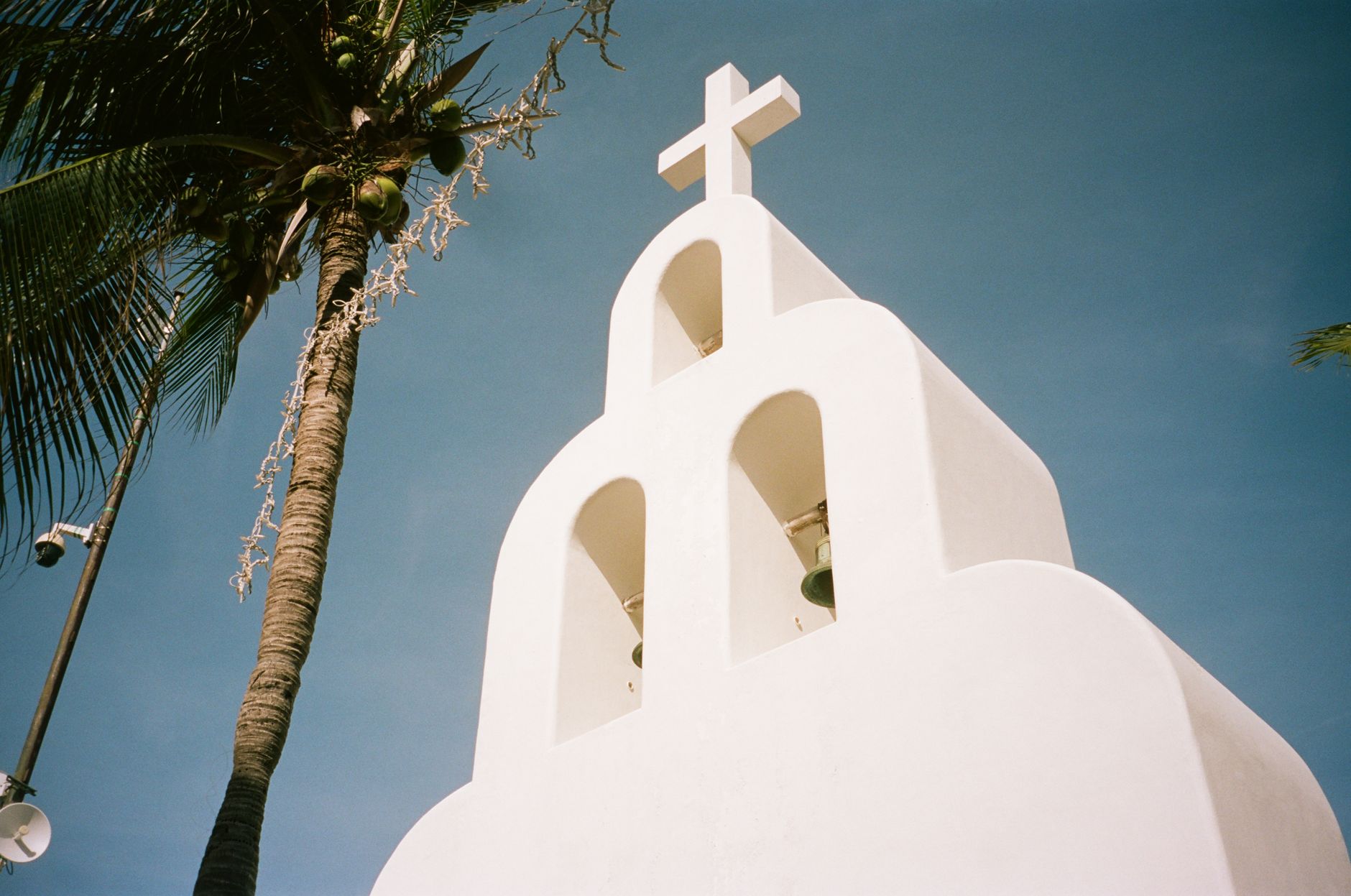A striking image of a white church tower and palm tree in Tulum, Mexico, under a clear blue sky.