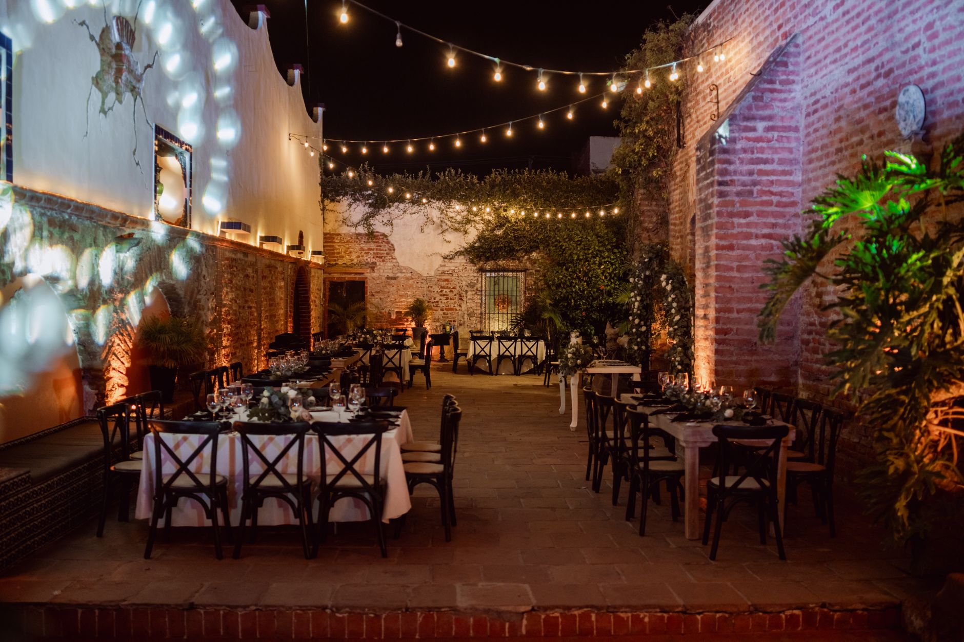Charming outdoor event setting at night, featuring tables with elegant decor under warm string lights.