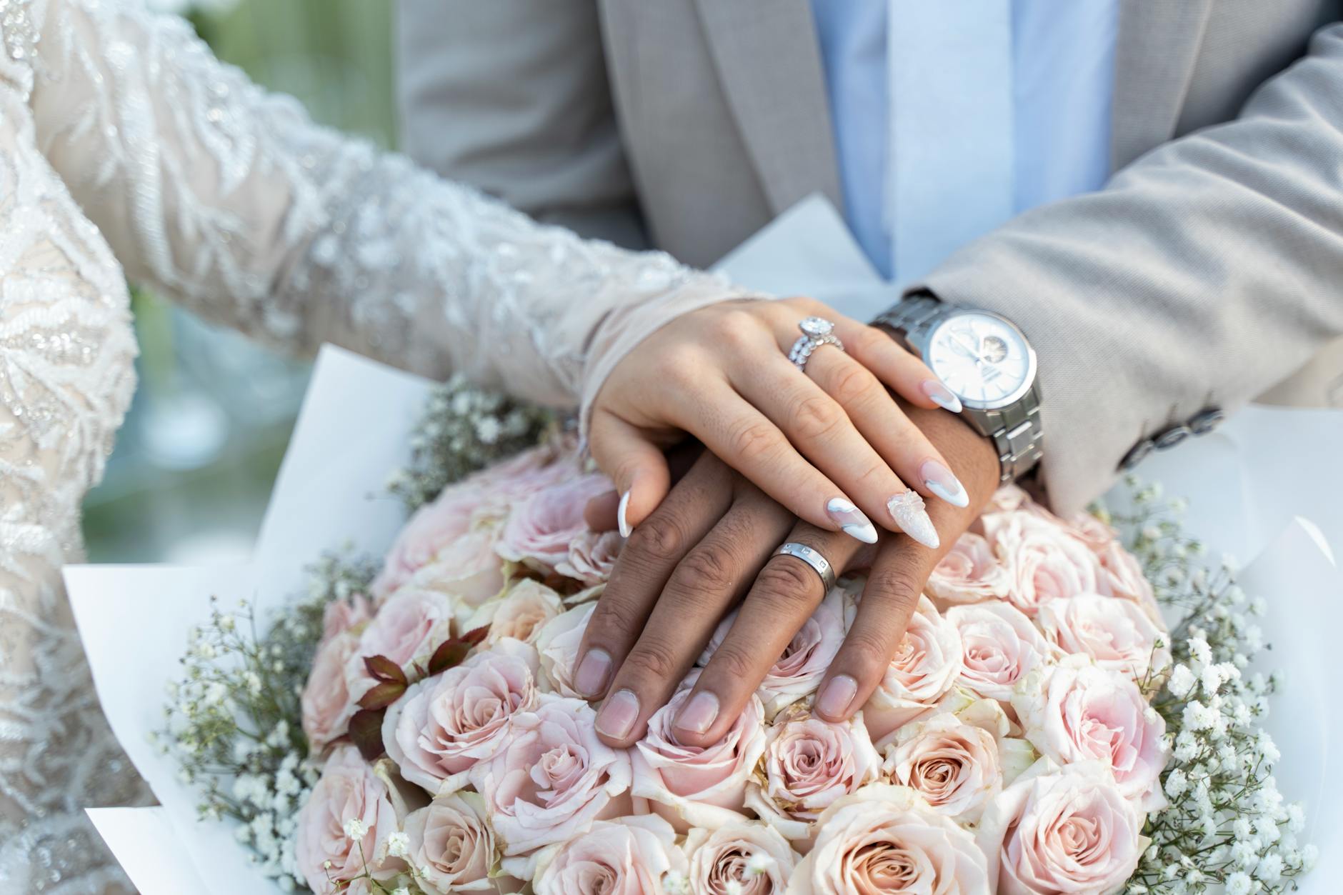 Close-up of elegant hands with wedding rings over a pastel rose bouquet in Sydney.