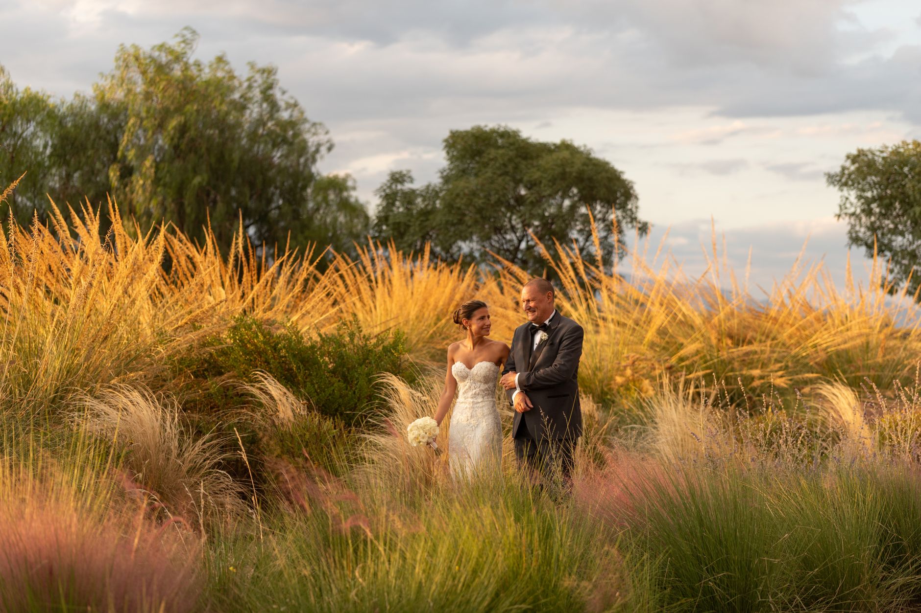 Bride and groom in elegant attire amidst a beautiful garden setting at sunset.