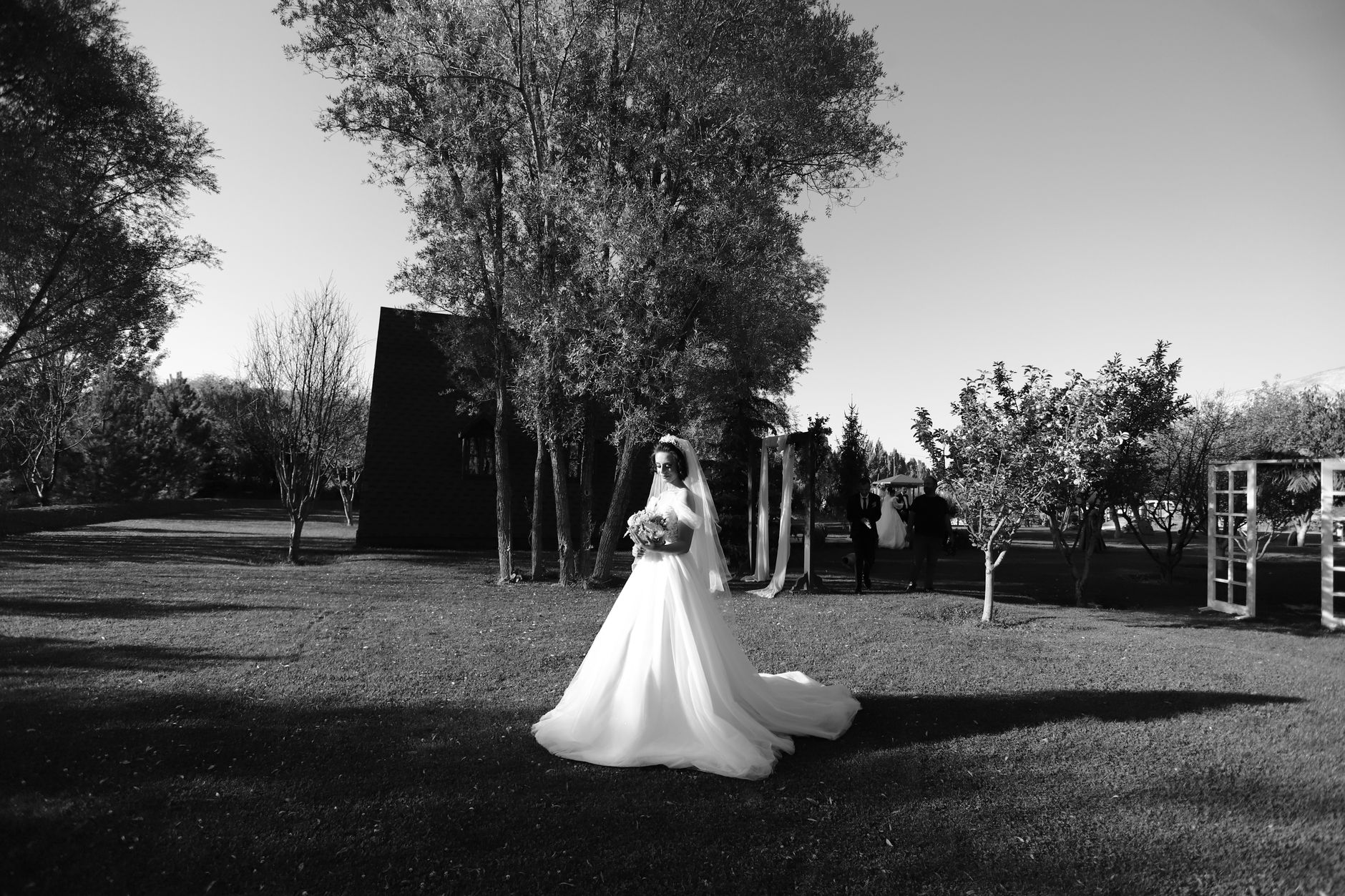 A bride in a wedding dress stands gracefully in a garden, captured in black and white.