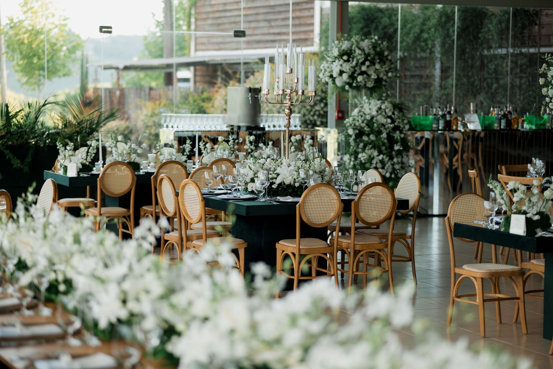 Chic event decoration with floral arrangements and wooden chairs in a bright sunlit room.