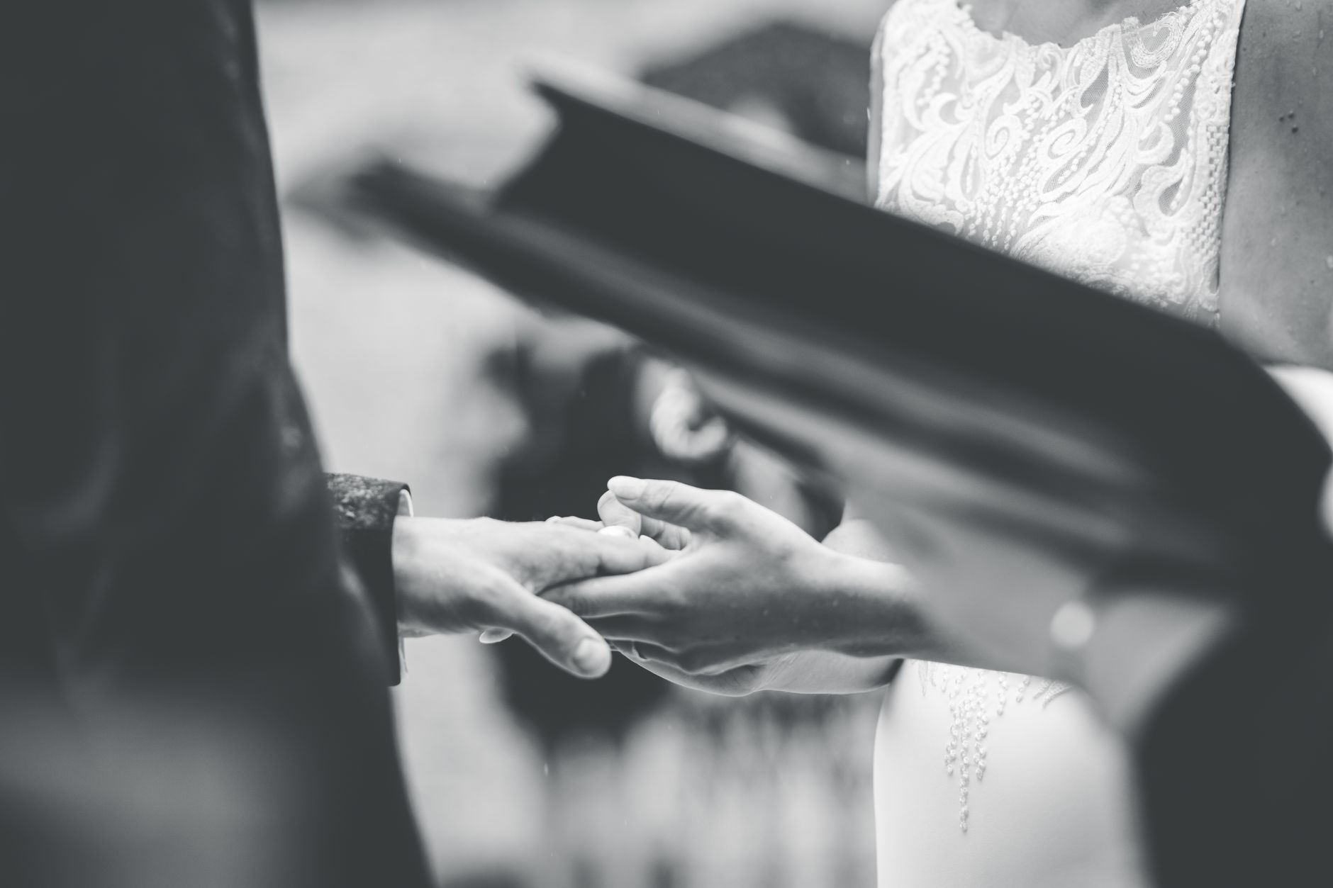 A touching black and white photo capturing the moment a bride and groom exchange rings during a wedding ceremony.