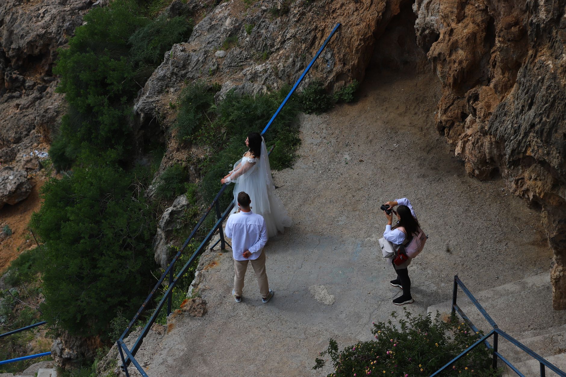 Bride and groom pose on a scenic cliff for a photographer during a wedding photo session.