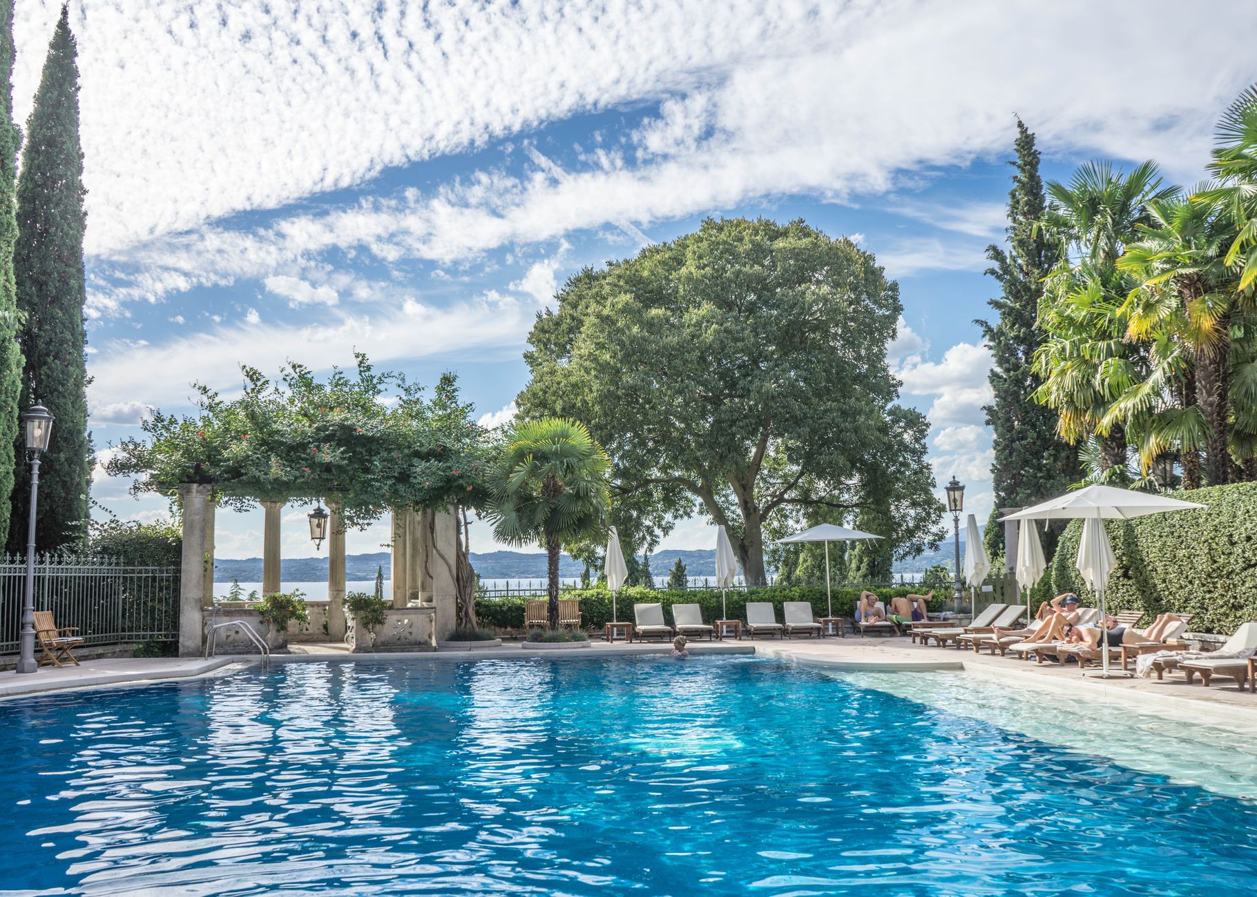 Enjoy a serene day by the luxurious tropical resort poolside, surrounded by palm trees and clear blue skies.