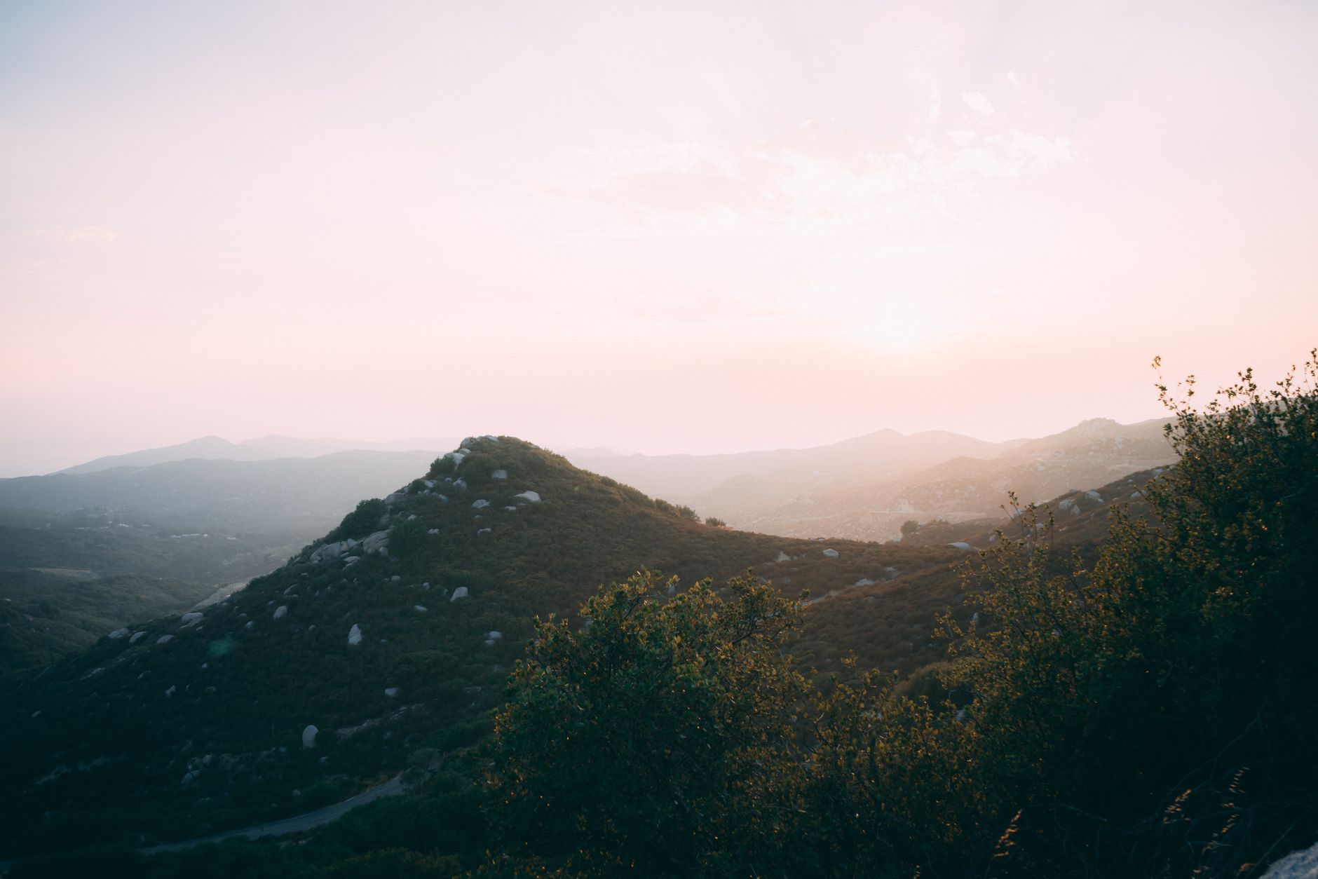 A picturesque view of mountains under a dramatic sky at sunrise, showcasing lush greenery.