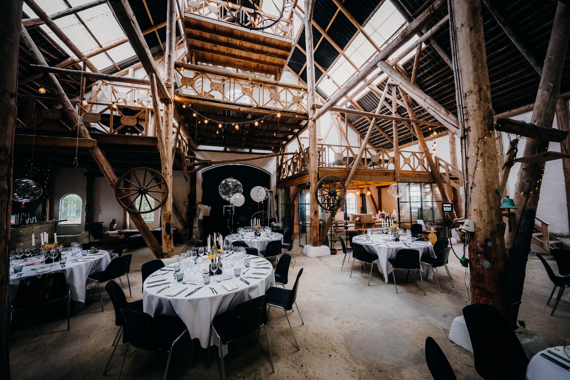 Interior view of a rustic barn converted into an elegant dining area with round tables set for an event.