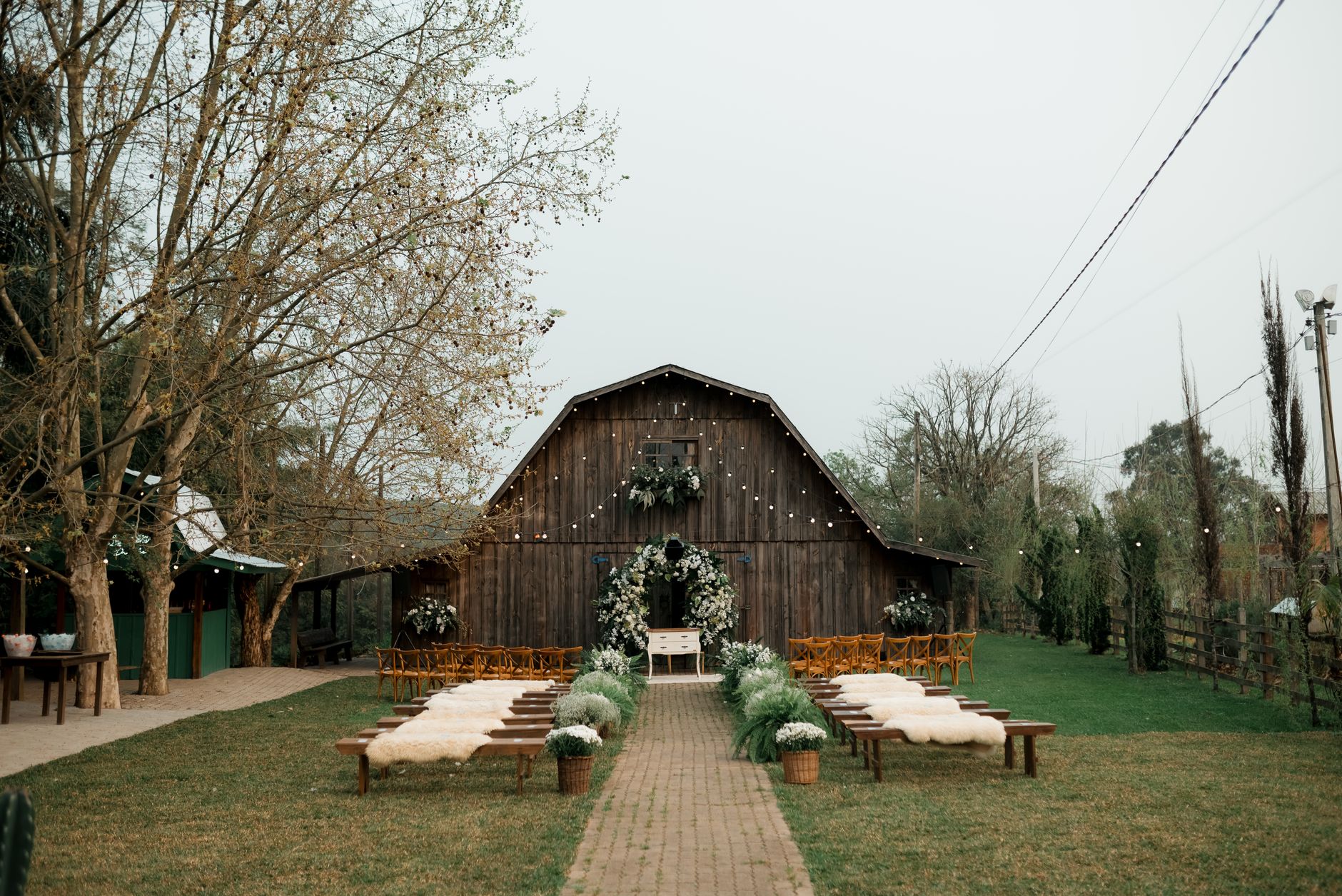 Rustic outdoor wedding venue with barn, floral decorations, and wooden benches.