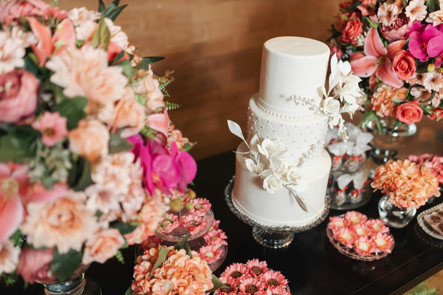 A white wedding cake surrounded by vibrant pink and orange floral arrangements, creating a luxurious setting.