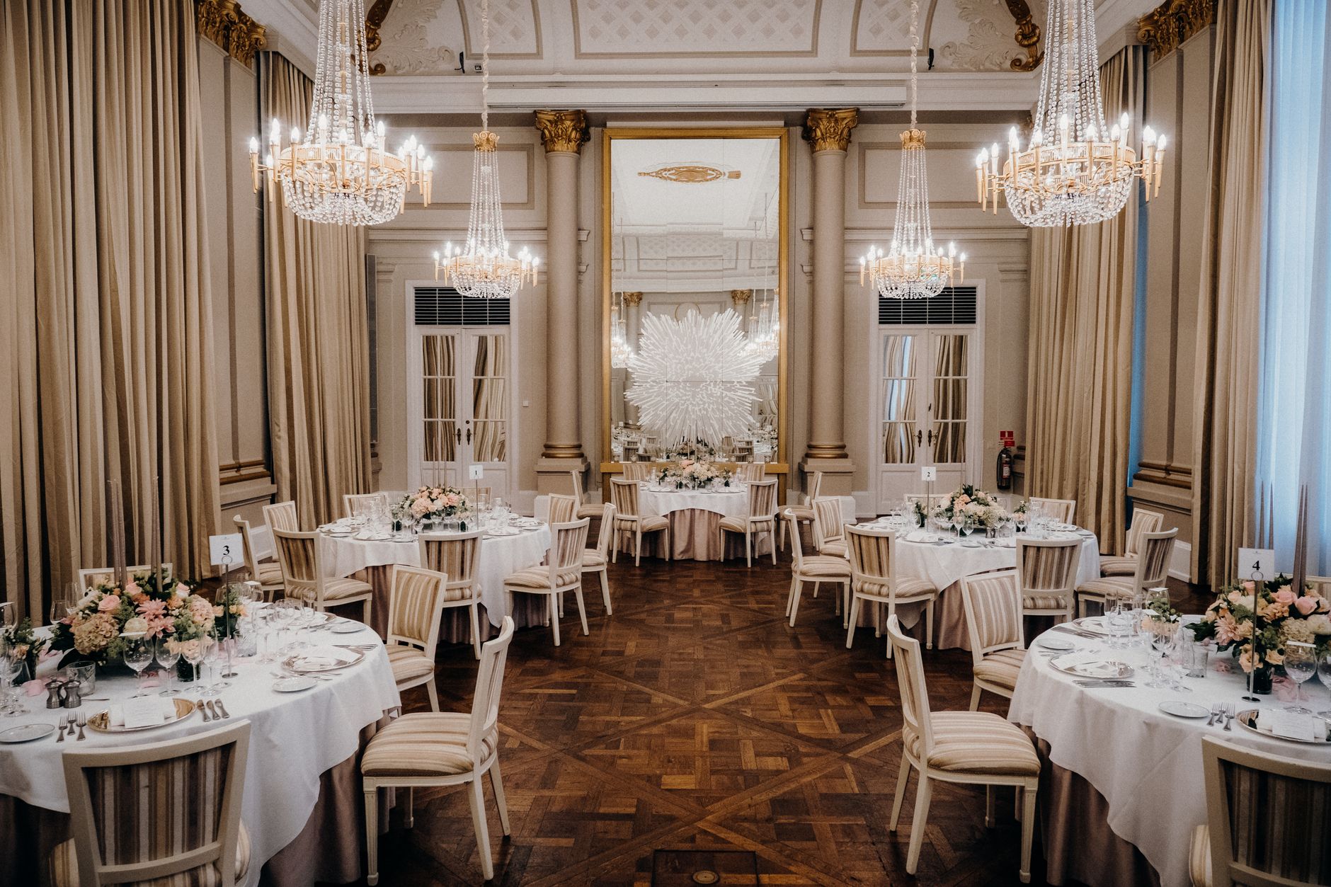 Luxurious banquet hall with elegant chandeliers and floral table settings, perfect for weddings.