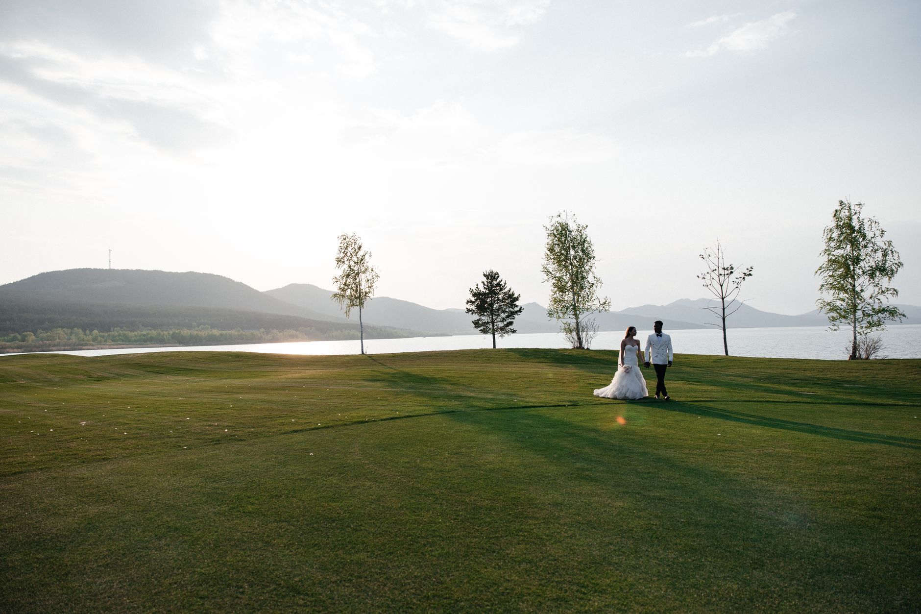 A bride and groom walking on a golf course by a lake in scenic Kazakhstan.