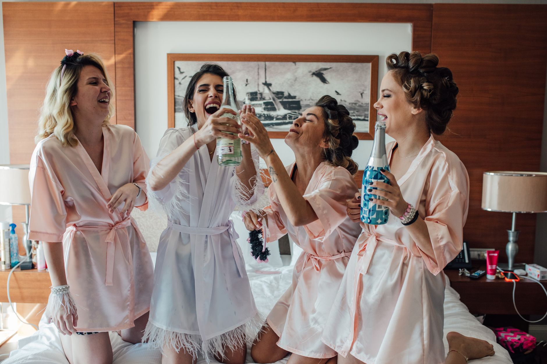 Bridal party in robes celebrating with champagne in a cozy hotel room setting.