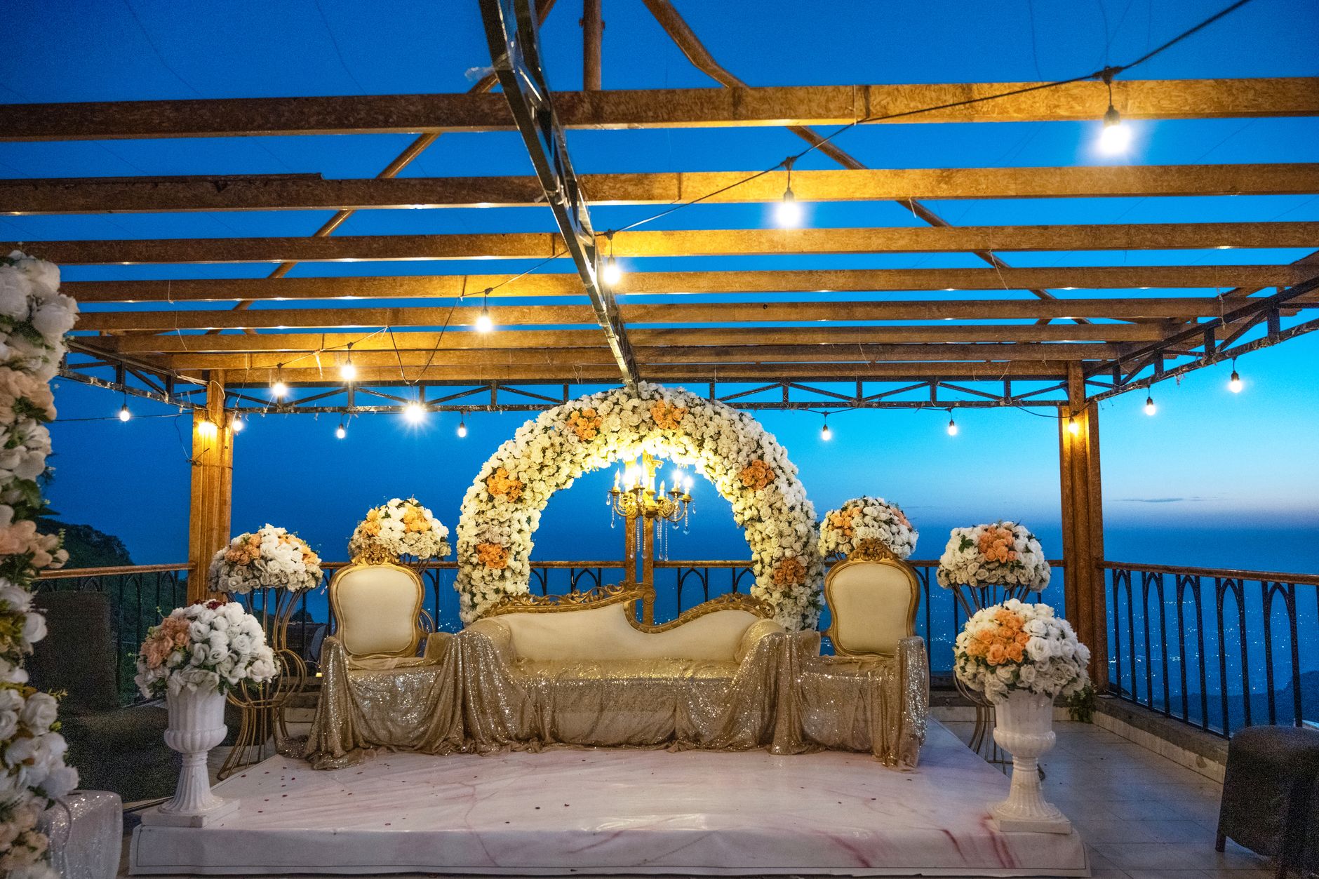 A beautifully decorated terrace with floral arrangements and string lights, perfect for an elegant outdoor event.