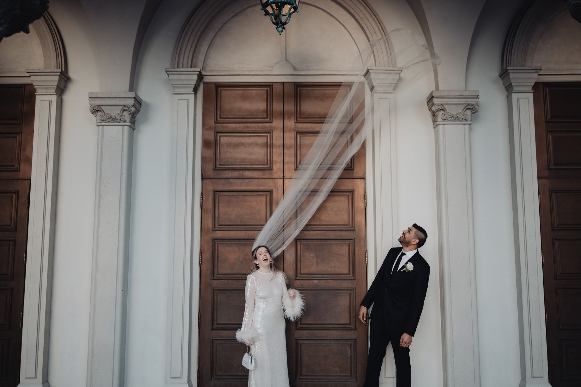 A joyful bride and groom pose playfully in front of elegant doors in Los Angeles.