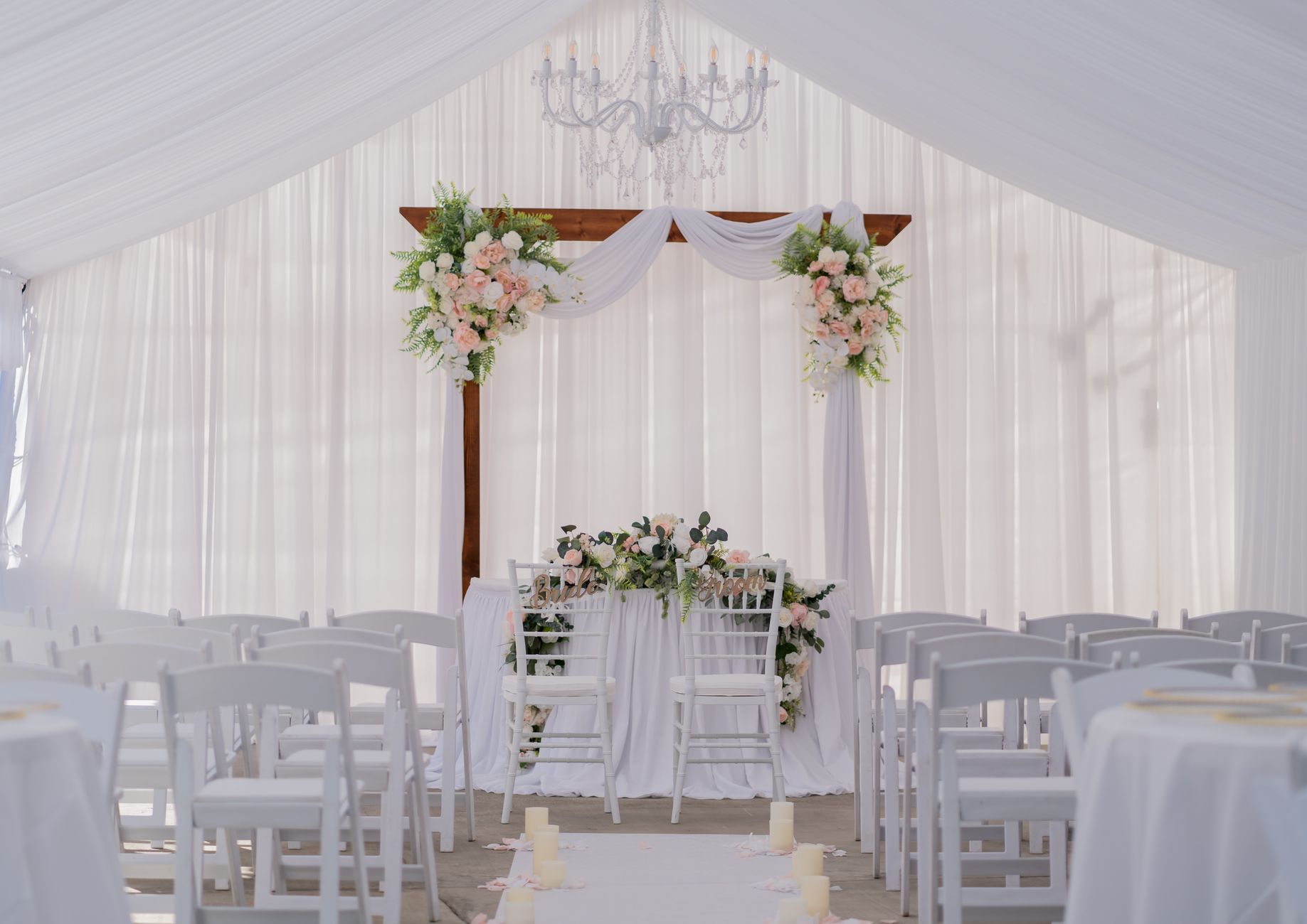 Beautiful wedding ceremony setup with white drapery, floral arrangements, and chandelier. Perfect for elegant nuptials.