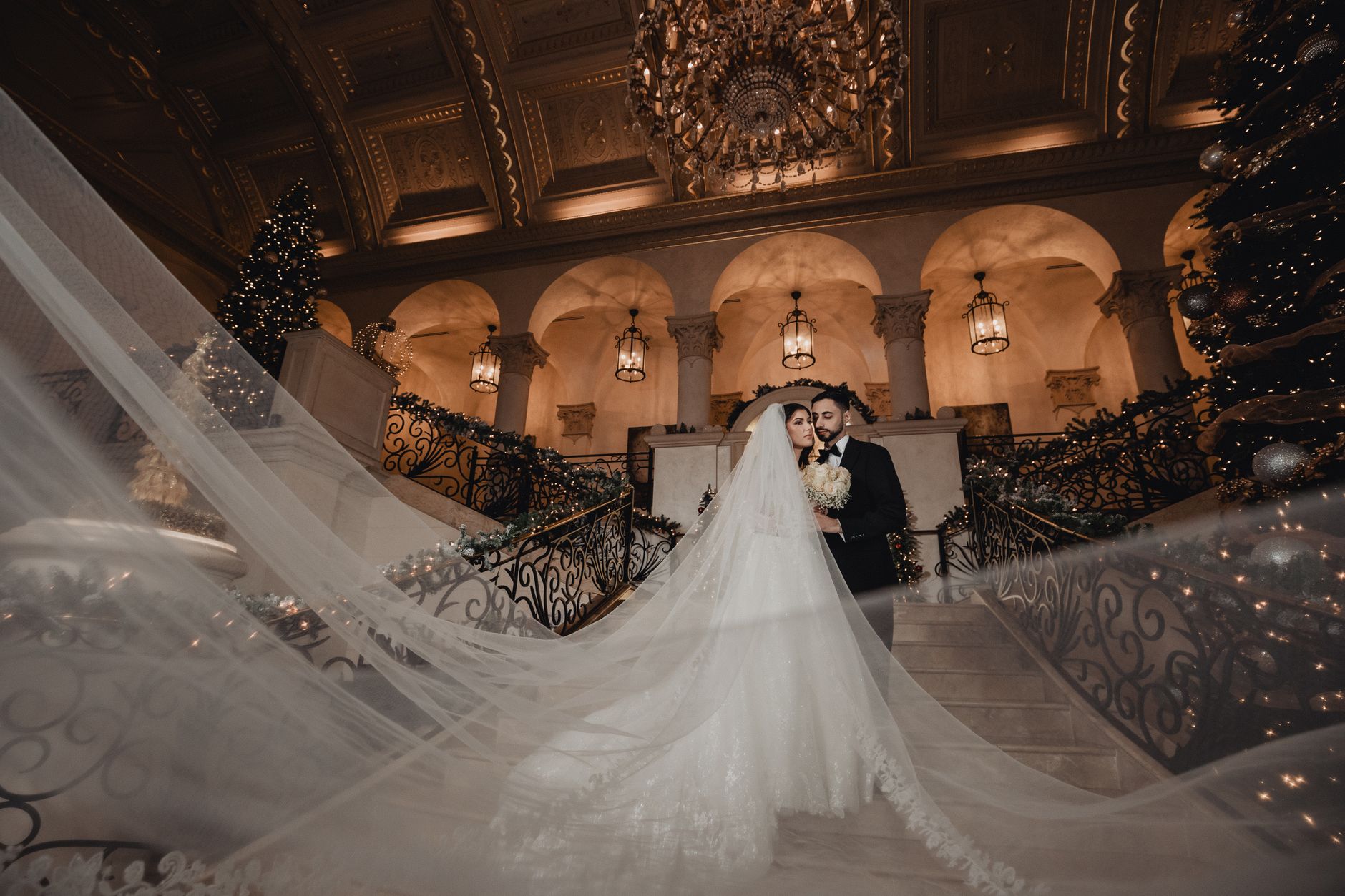 Romantic wedding portrait of a couple in an opulent indoor setting with a flowing veil.