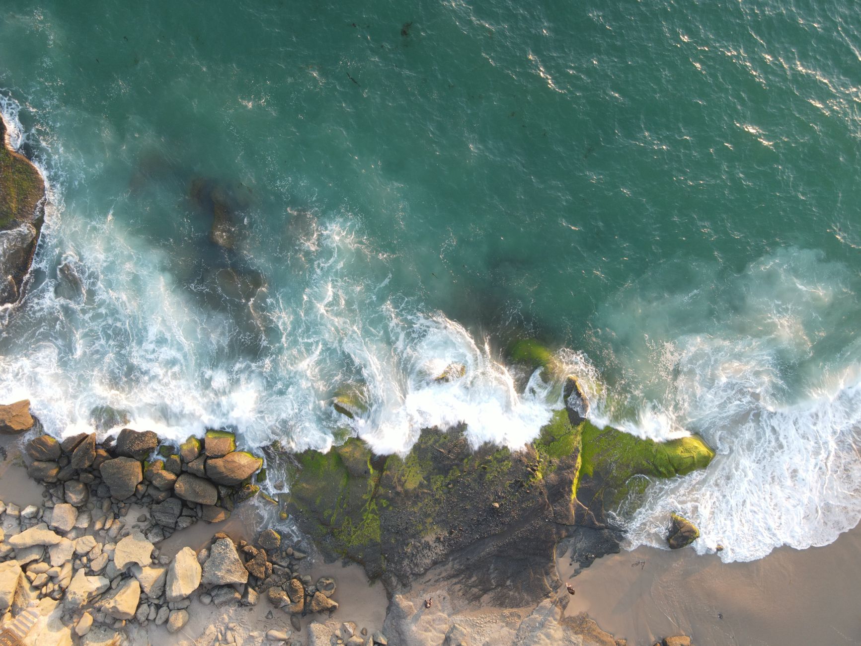 Dramatic aerial shot of rocky seashore with waves crashing in Laguna Beach, California.