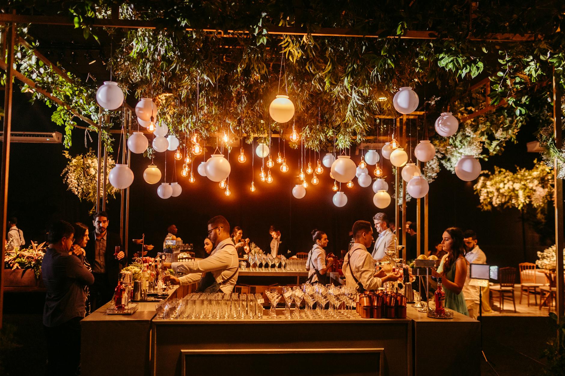 A stylish wedding reception showcasing a beautifully decorated bar with ambient lighting and lush greenery.