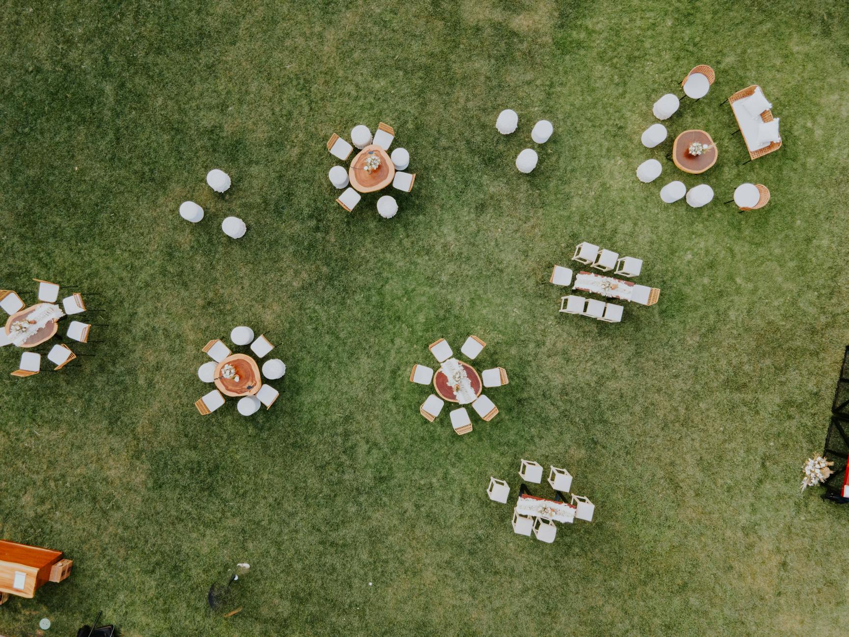 Top-down view of outdoor event tables and chairs neatly arranged on green grass.