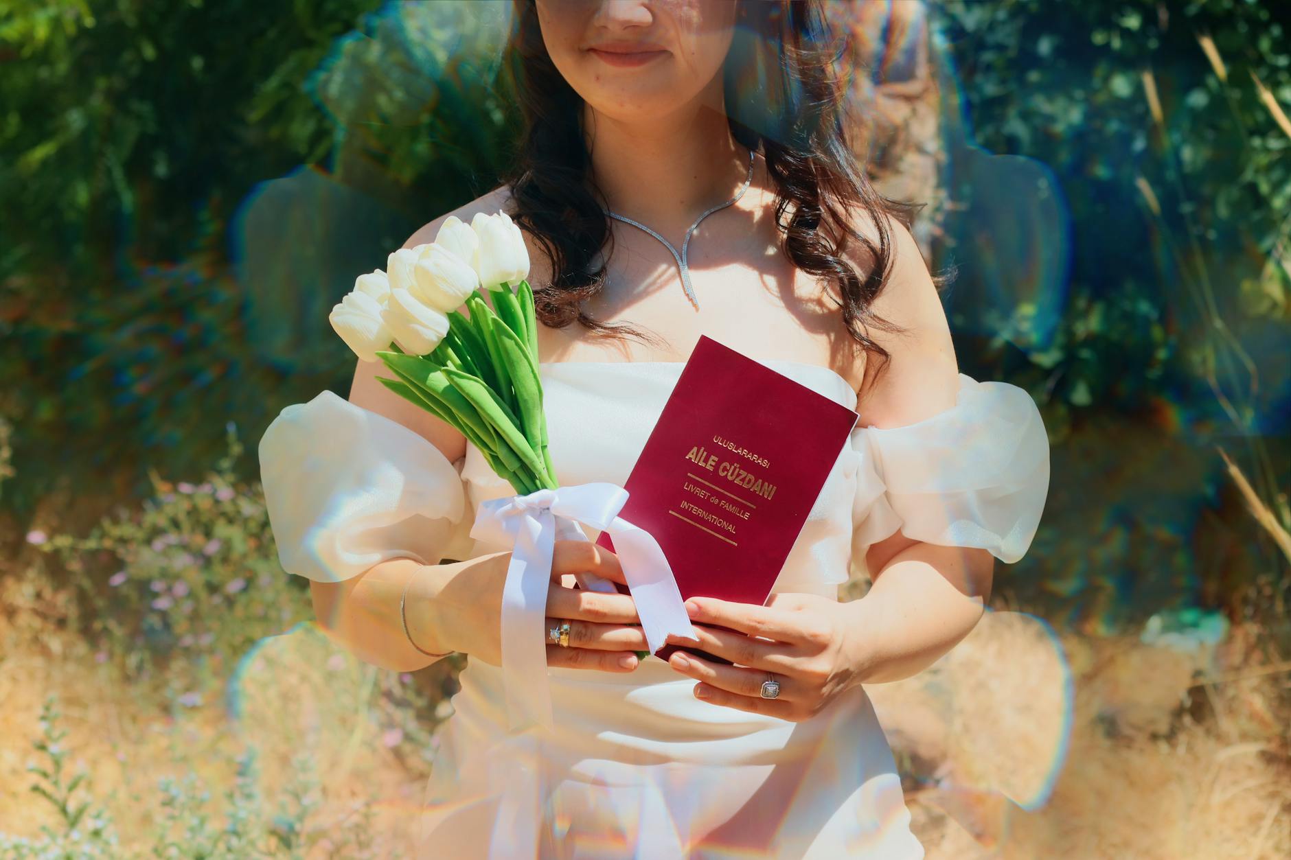 Bride in white dress holding a wedding passport and white tulips outdoors.