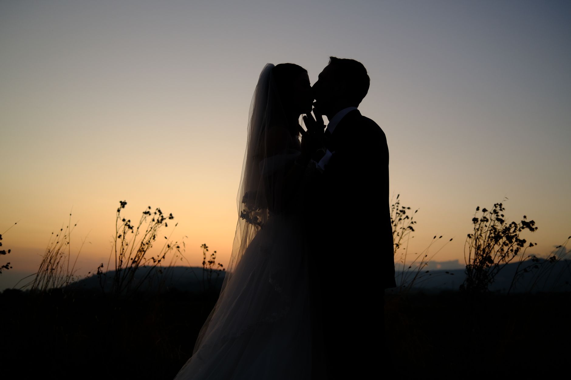 A romantic silhouette of a couple kissing during sunset on their wedding day, outdoors.