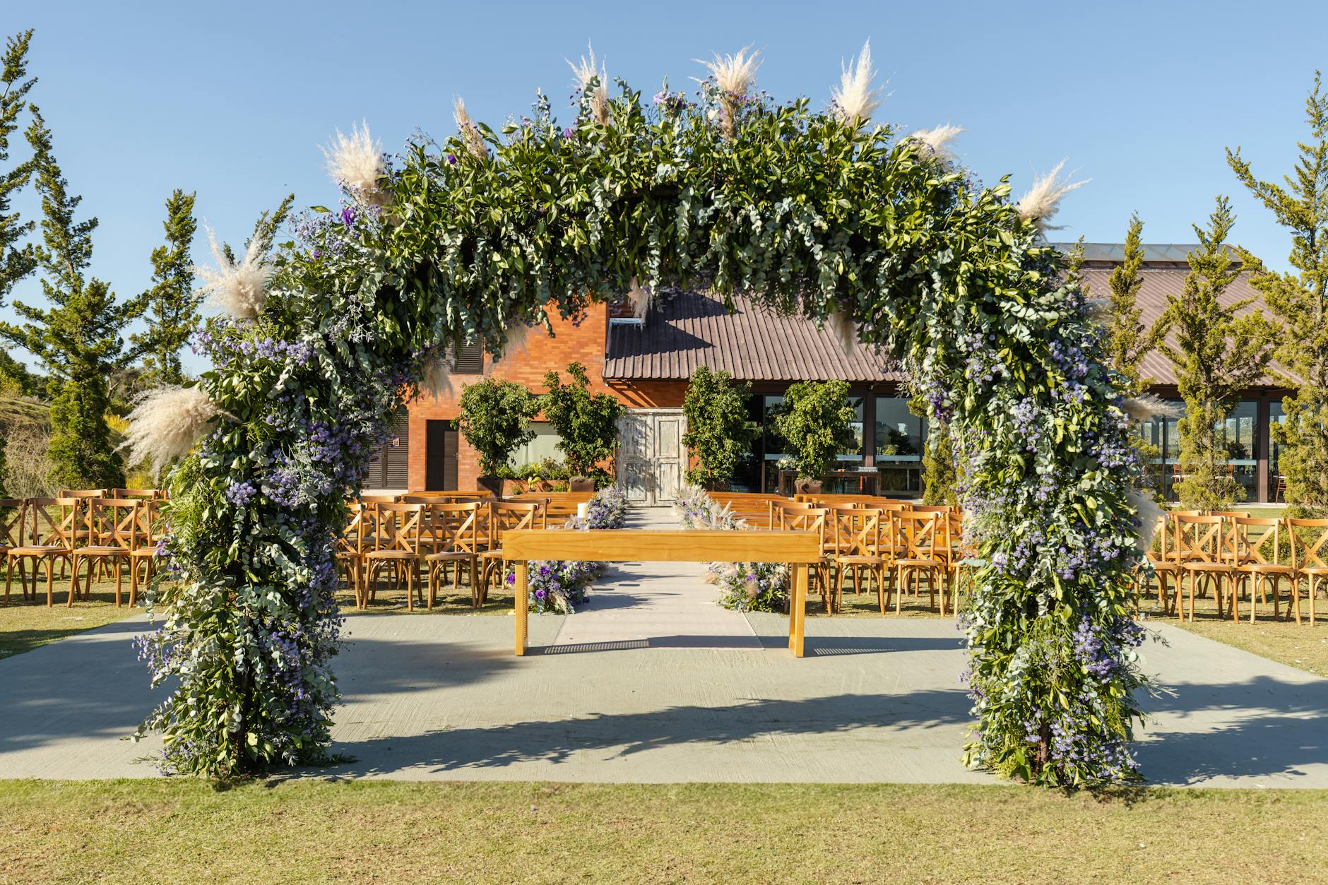 Stunning outdoor wedding setup with a floral arbor and rustic chairs under clear blue sky.