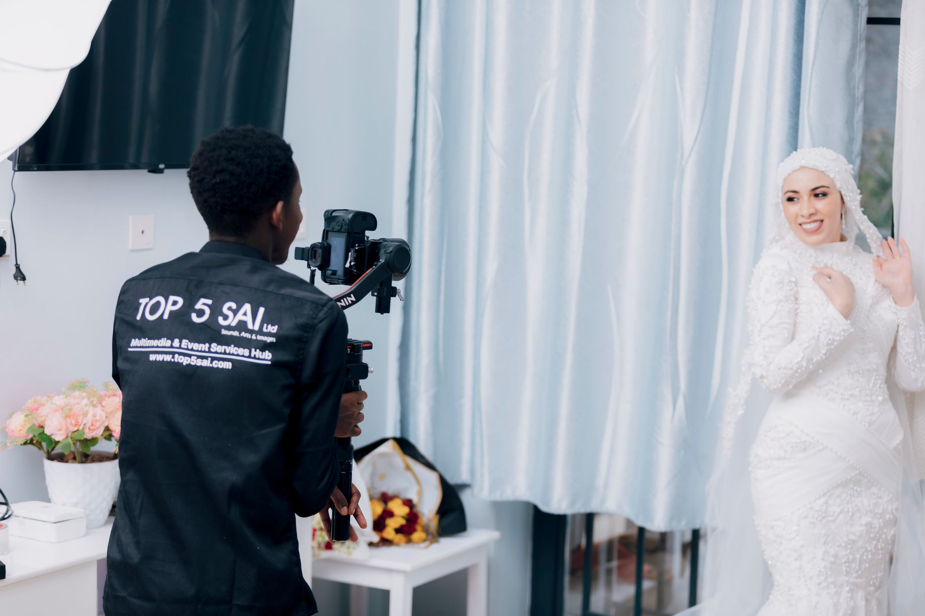 Bride in white dress poses for photographer during a wedding photoshoot indoors.