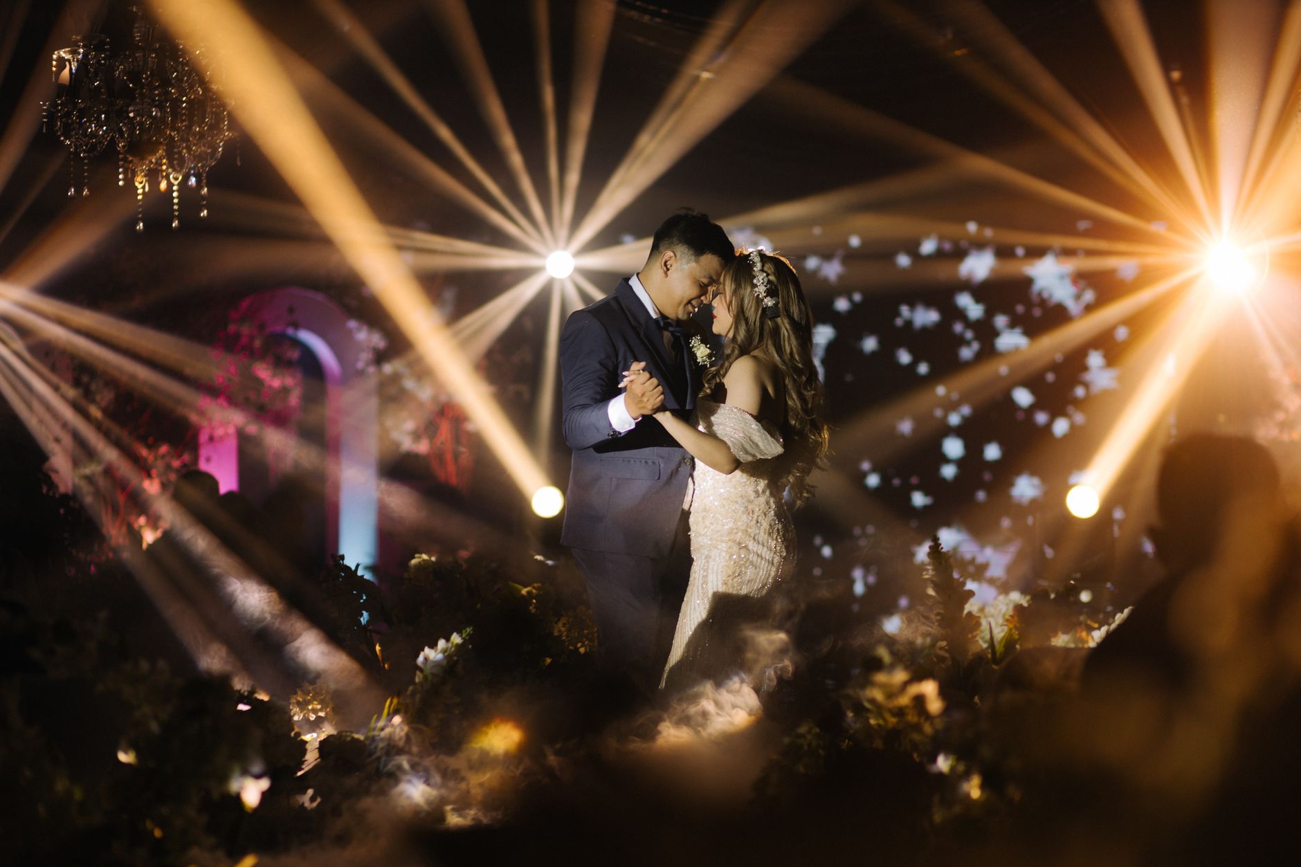 A bride and groom share a romantic dance amidst dramatic spotlights at a wedding celebration.