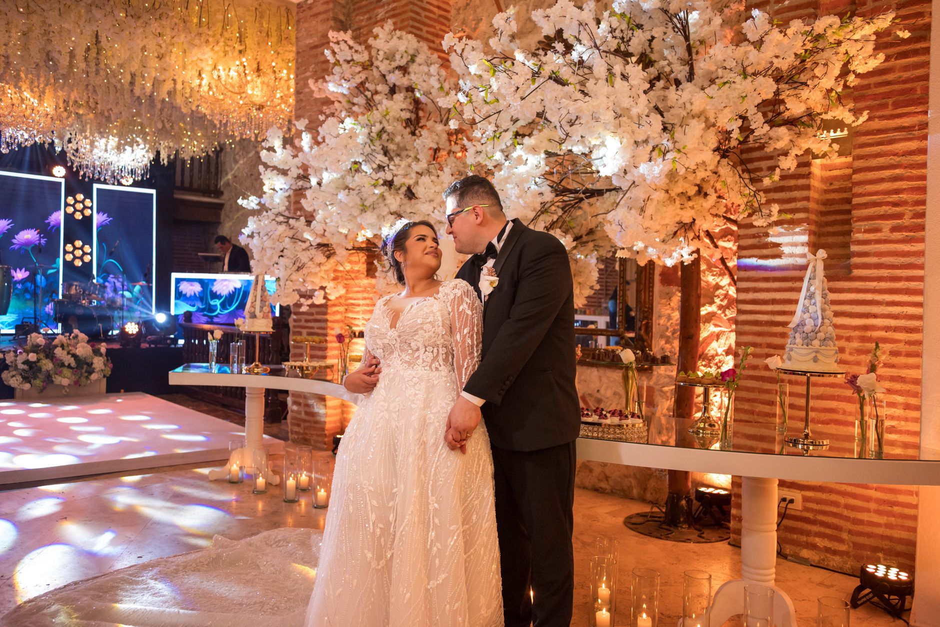 A couple in wedding attire embraces at an elegant reception, surrounded by floral decor.
