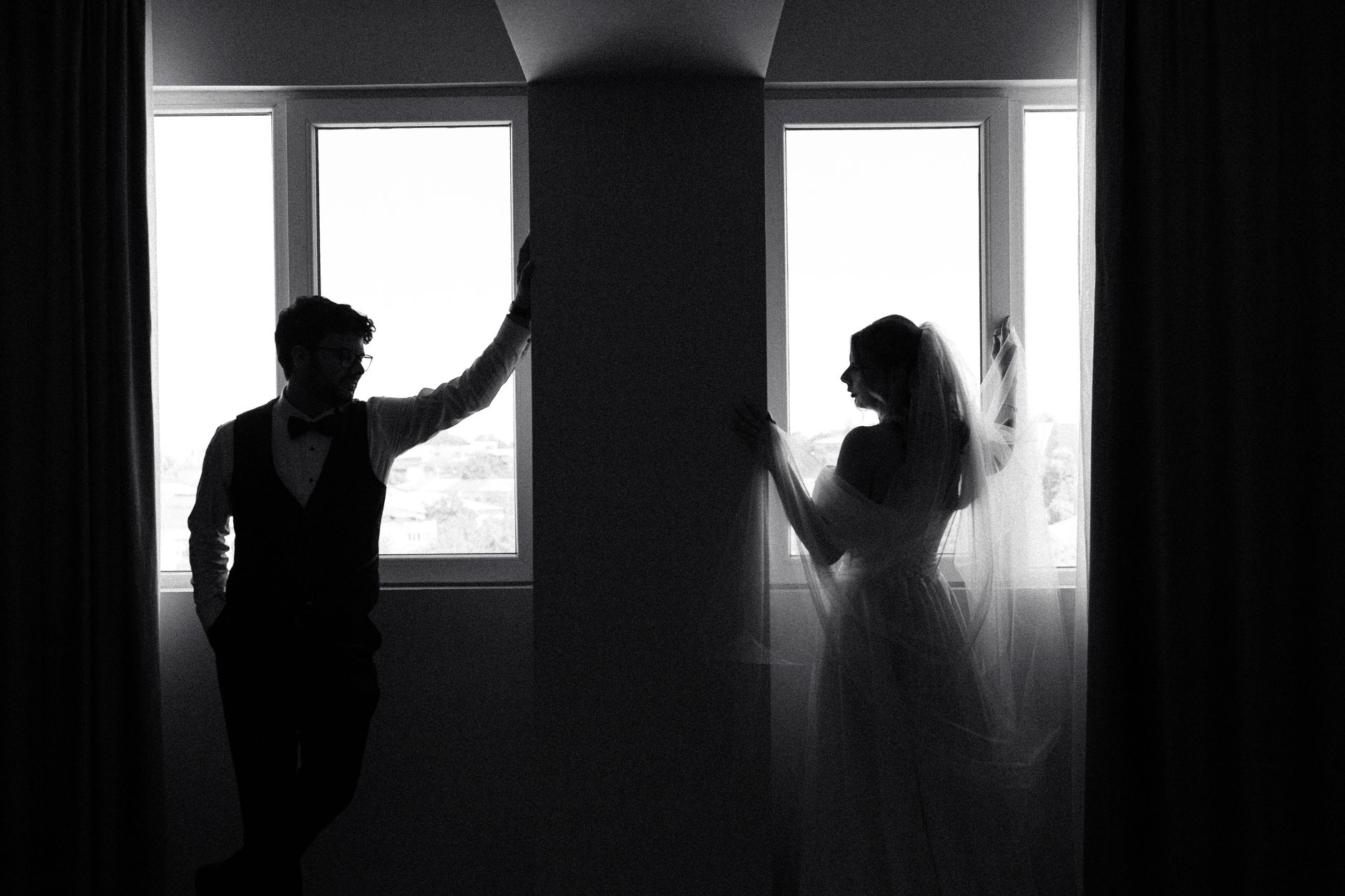 Black and white silhouette of a bride and groom by a window, creating a timeless and elegant look.