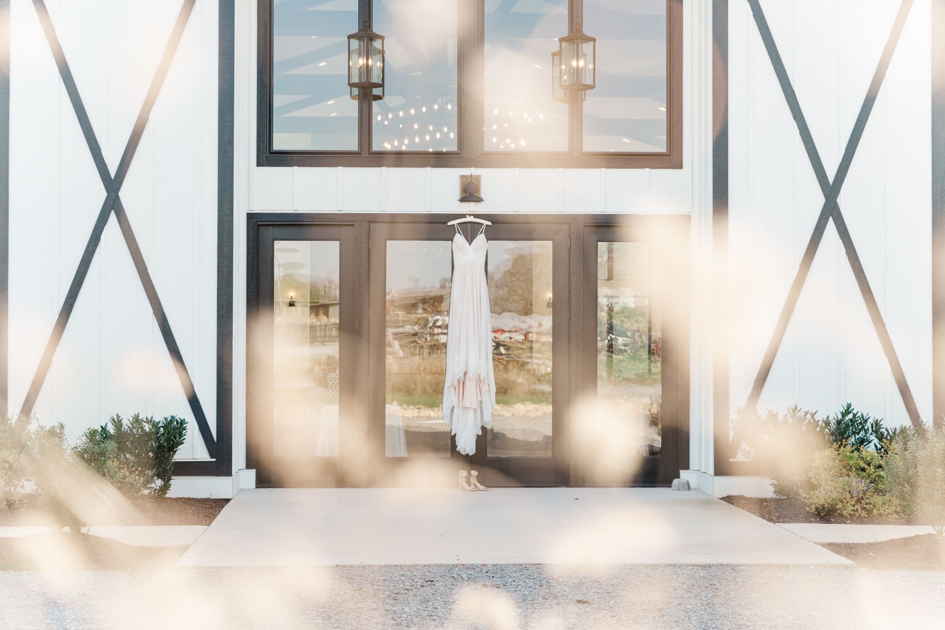 Elegant wedding dress hanging on a rustic barn door entrance with soft lighting.