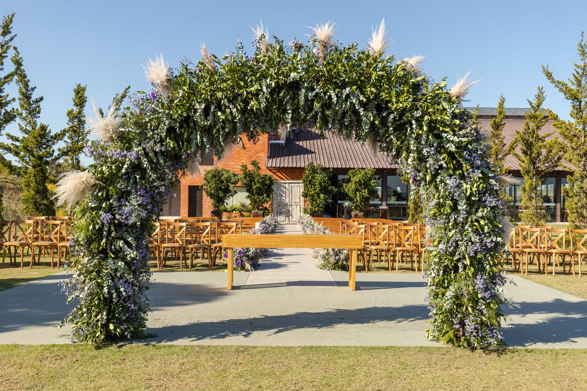 Stunning outdoor wedding setup with a floral arbor and rustic chairs under clear blue sky.
