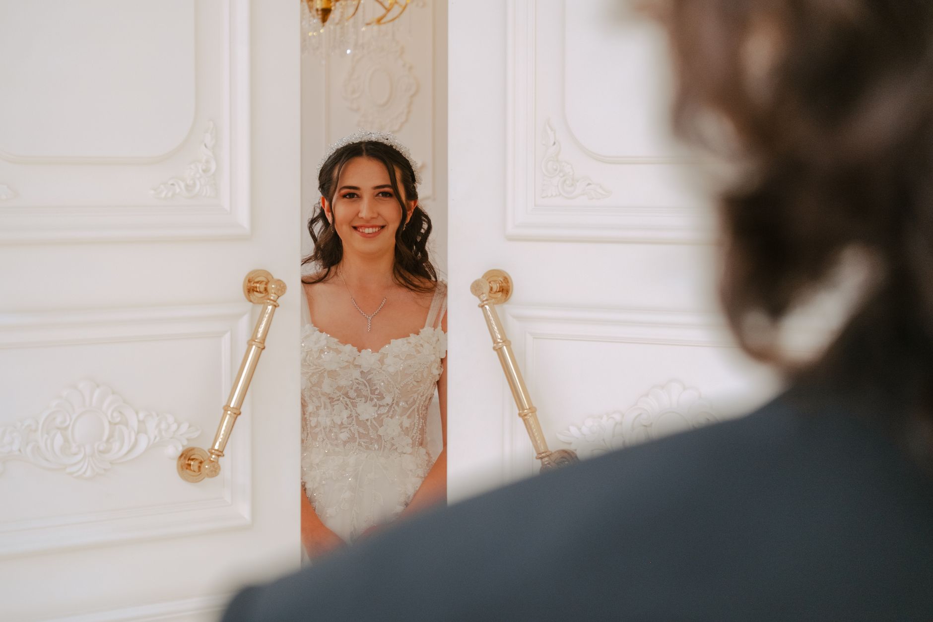 A beautiful bride in an elegant white gown smiles warmly while being greeted at a lavish wedding venue.