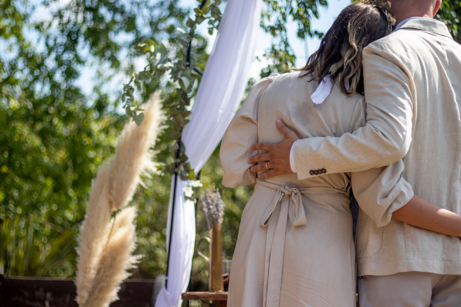 A couple embracing at an outdoor wedding ceremony under a decorative arch.