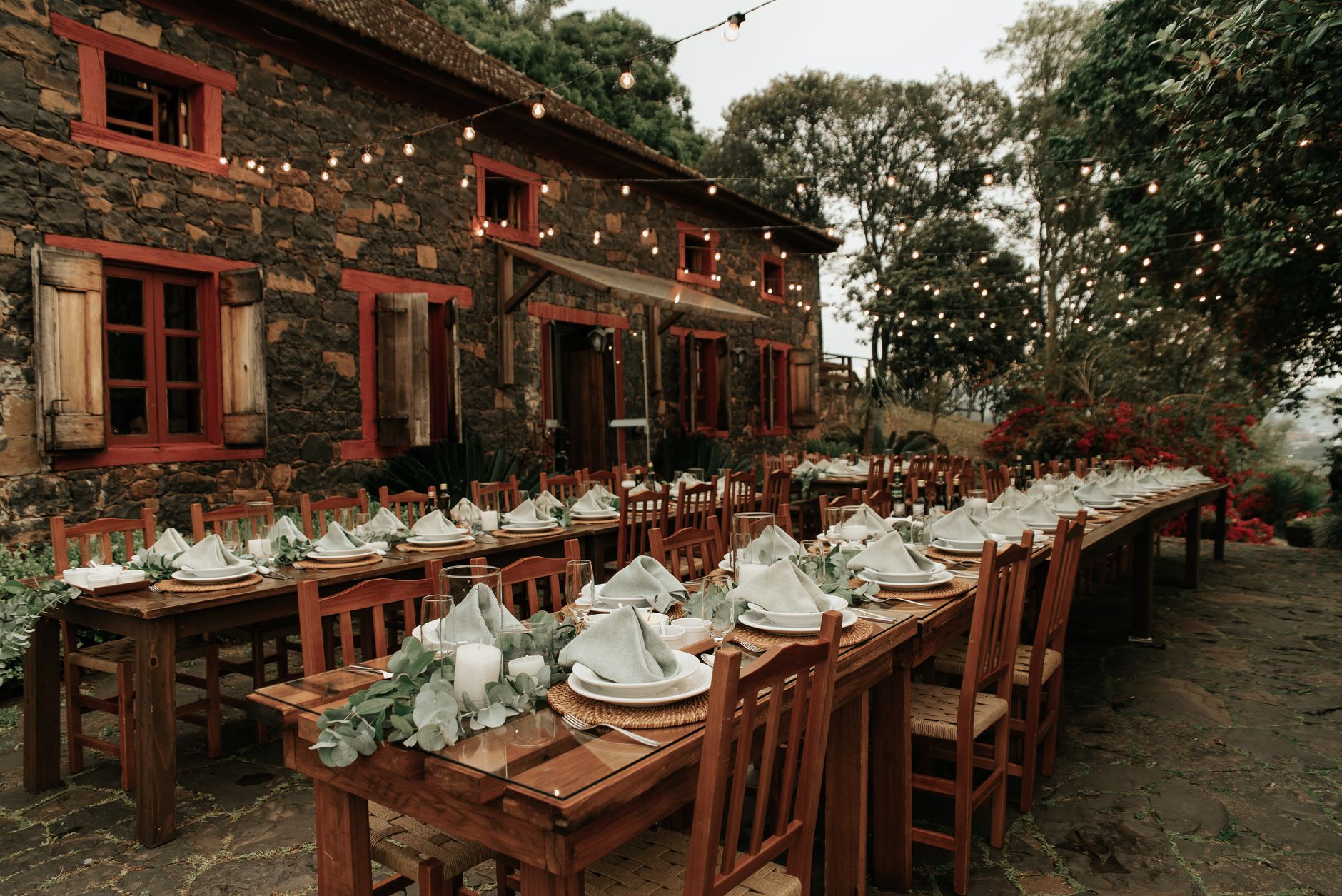 Charming outdoor dining setup with wooden tables and string lights at a rustic stone building.