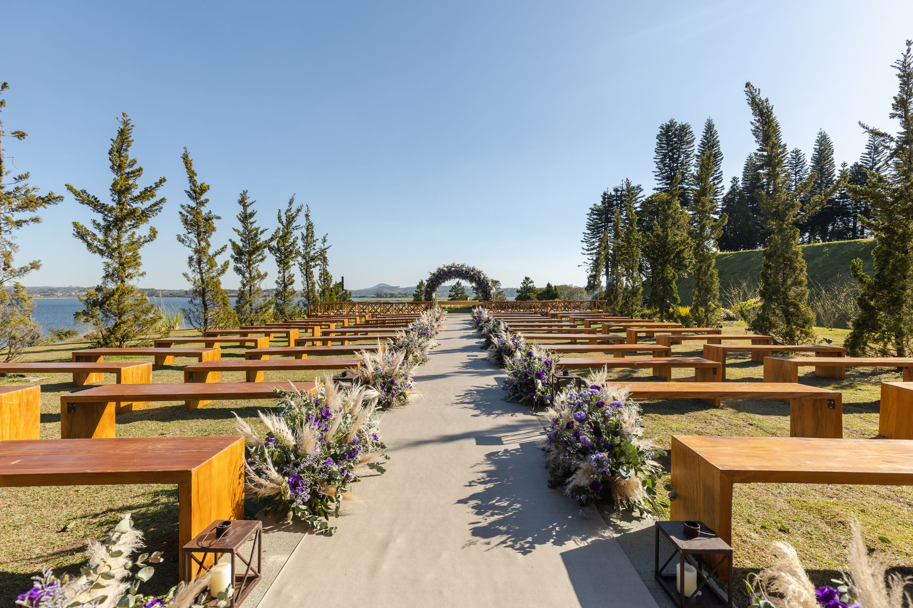 Charming outdoor wedding setup with wooden benches and floral decor by a serene lake.