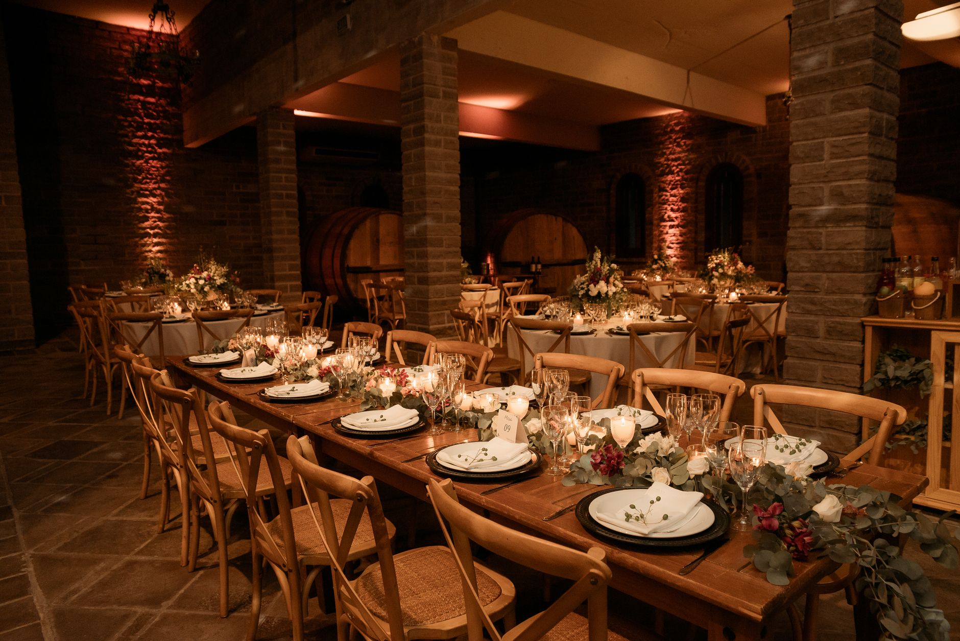 Beautifully set tables in a rustic winery for an elegant event with warm lighting and floral decor.